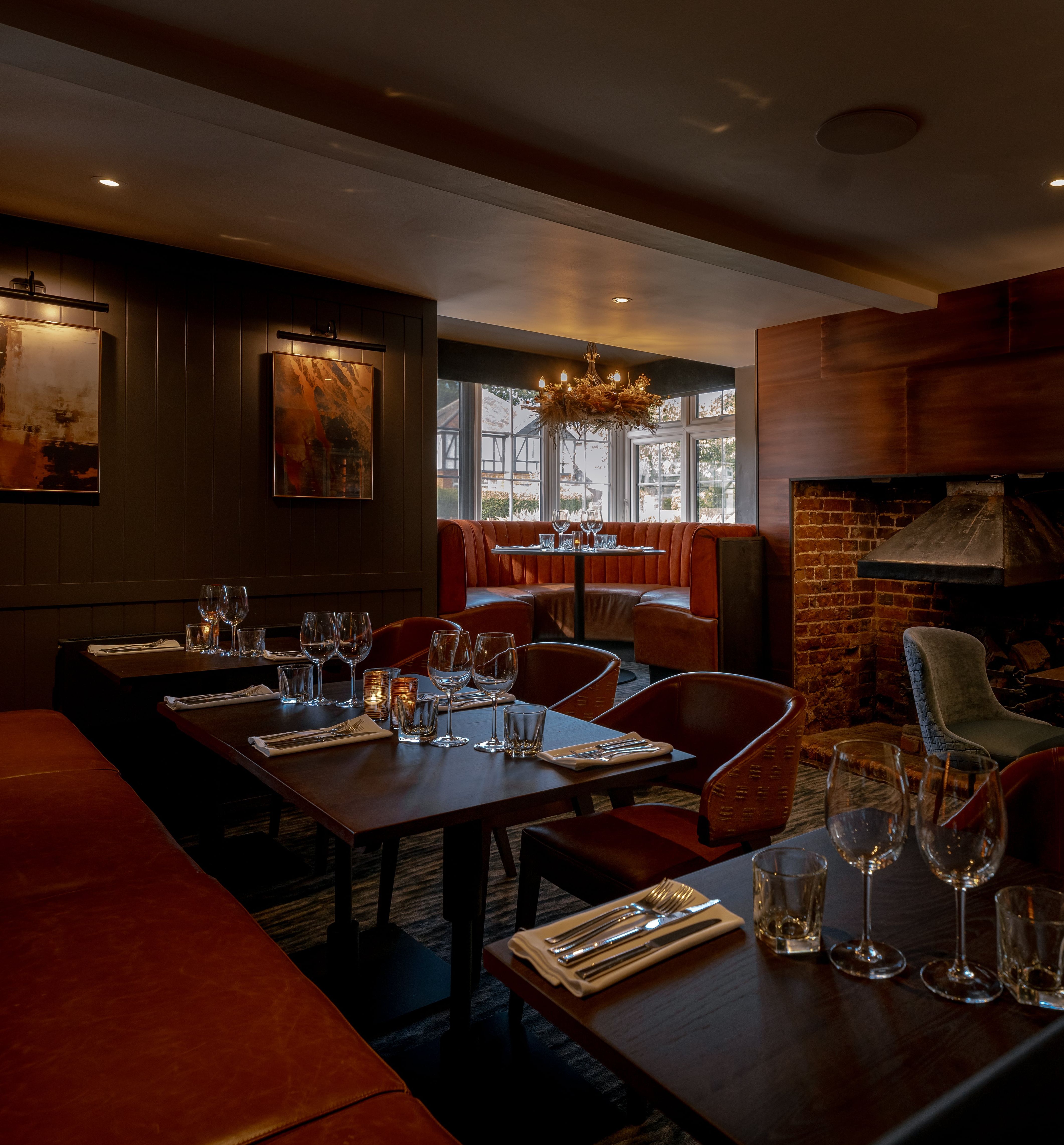 Elegant restaurant interior with brown leather seating, set tables, modern lighting, and a brick fireplace.