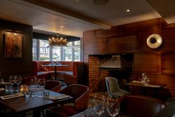 Cozy restaurant interior with set tables, leather seating, a fireplace, and warm lighting.
