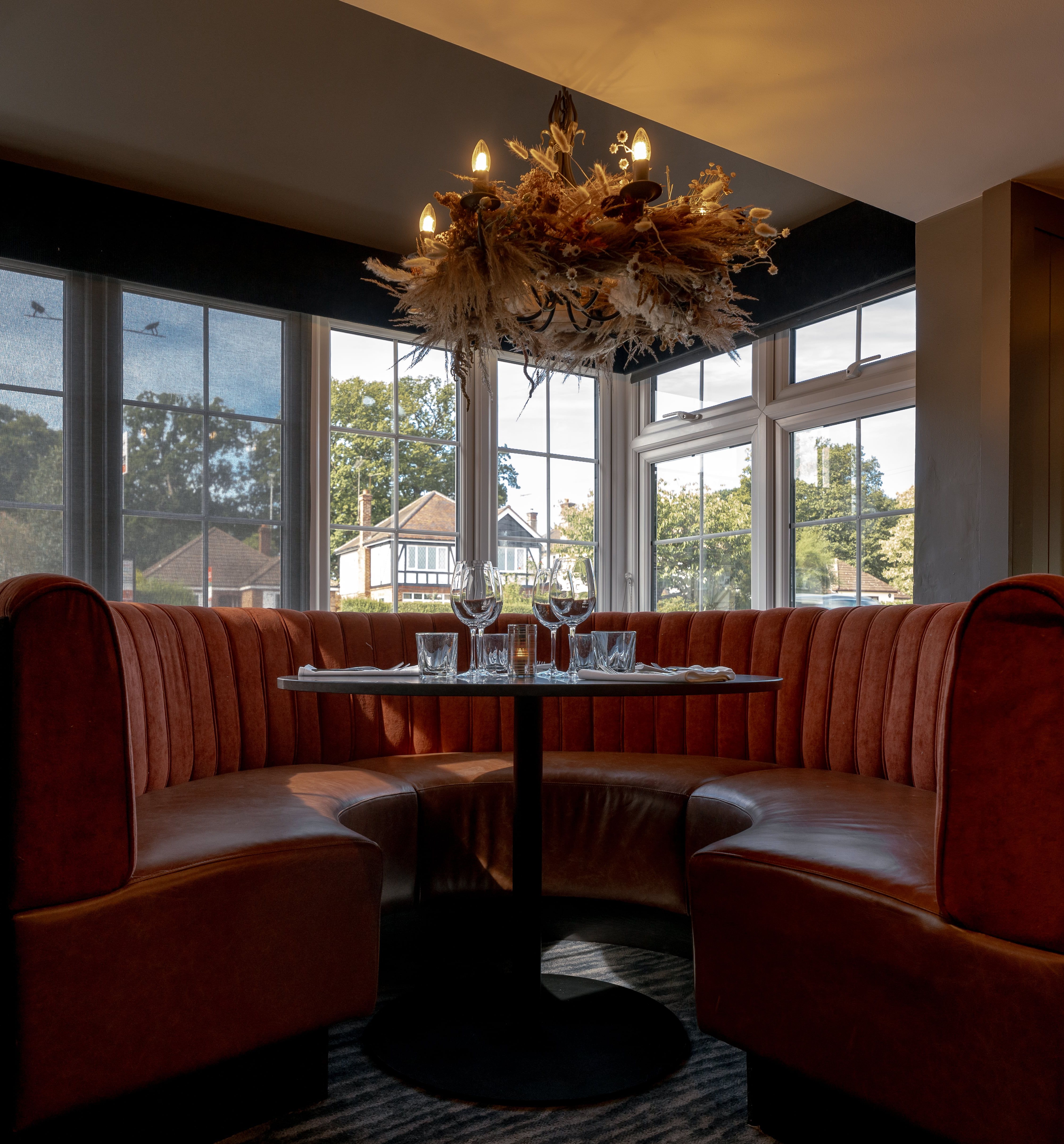 Cozy dining booth with red velvet seating, set table, and decorative chandelier in a restaurant