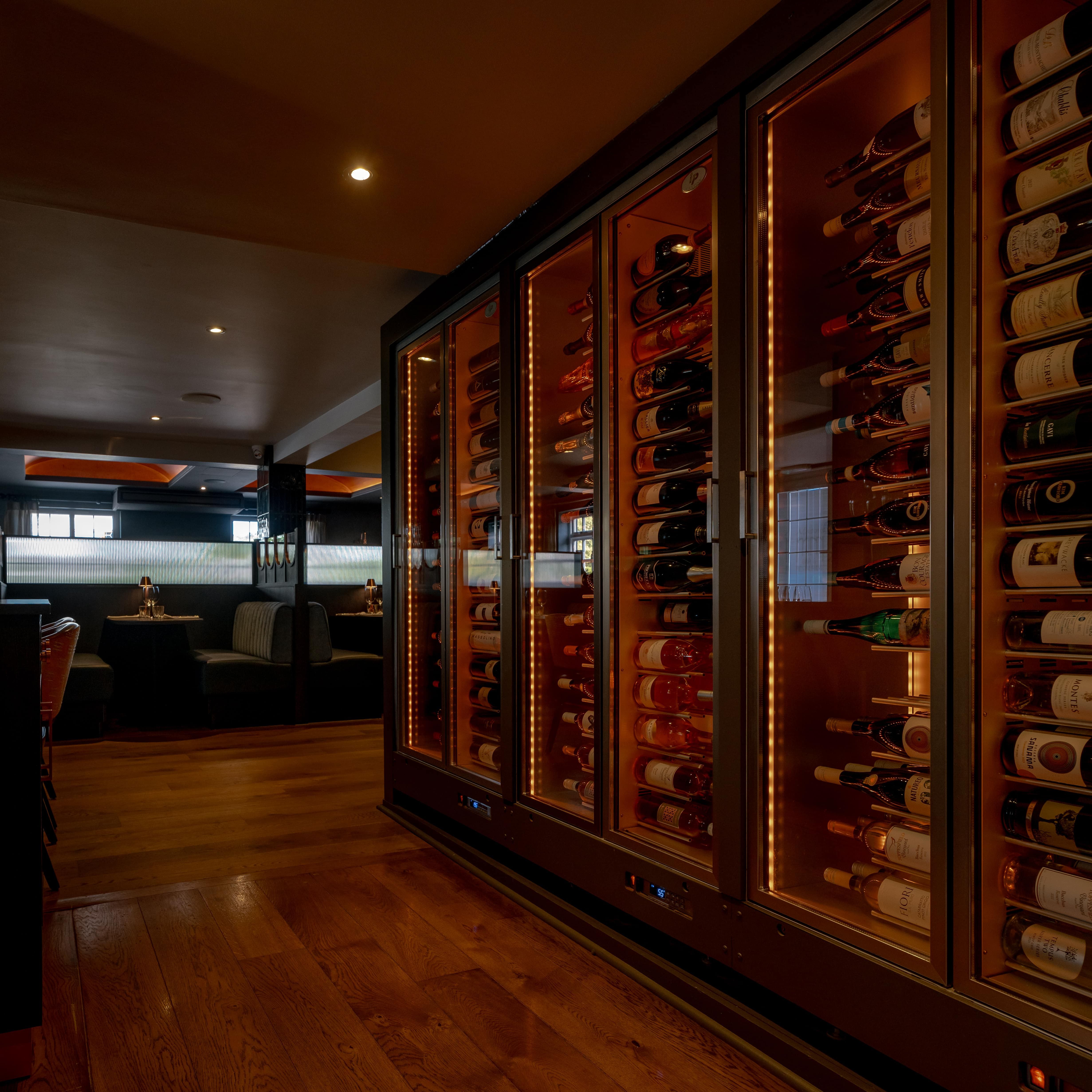 Modern restaurant interior with a large glass wine fridge stocked with bottles.