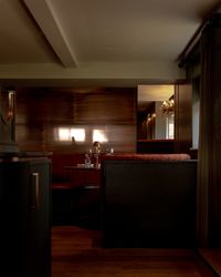 Intimate dining booth with curved banquette seating, set with glassware and a small table lamp in a dimly lit restaurant.