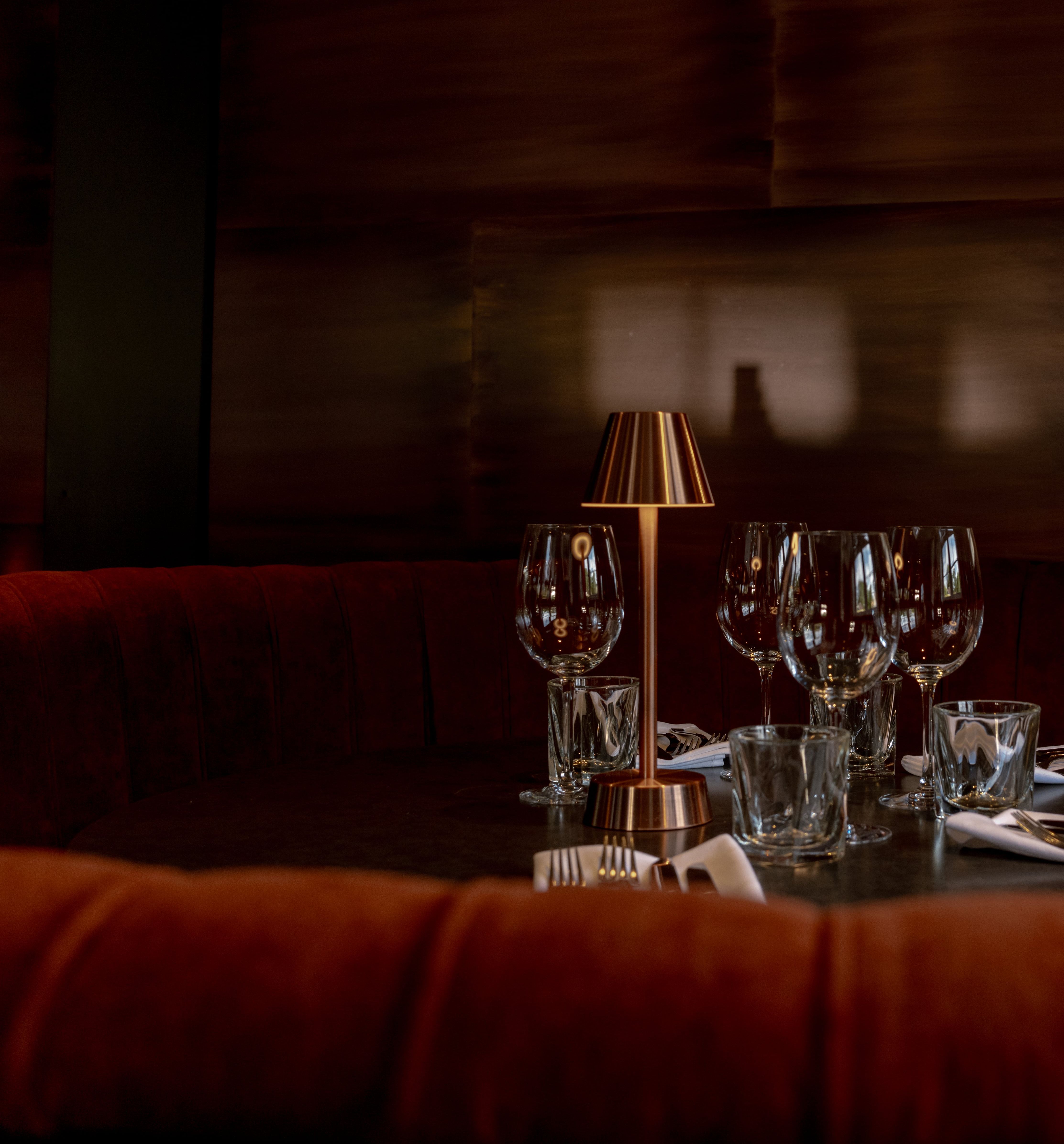 Elegant dining booth with red velvet seating, set table with glassware and a small lamp