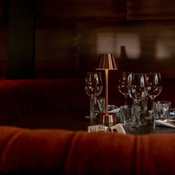 Elegant dining booth with red velvet seating, set table with glassware and a small lamp