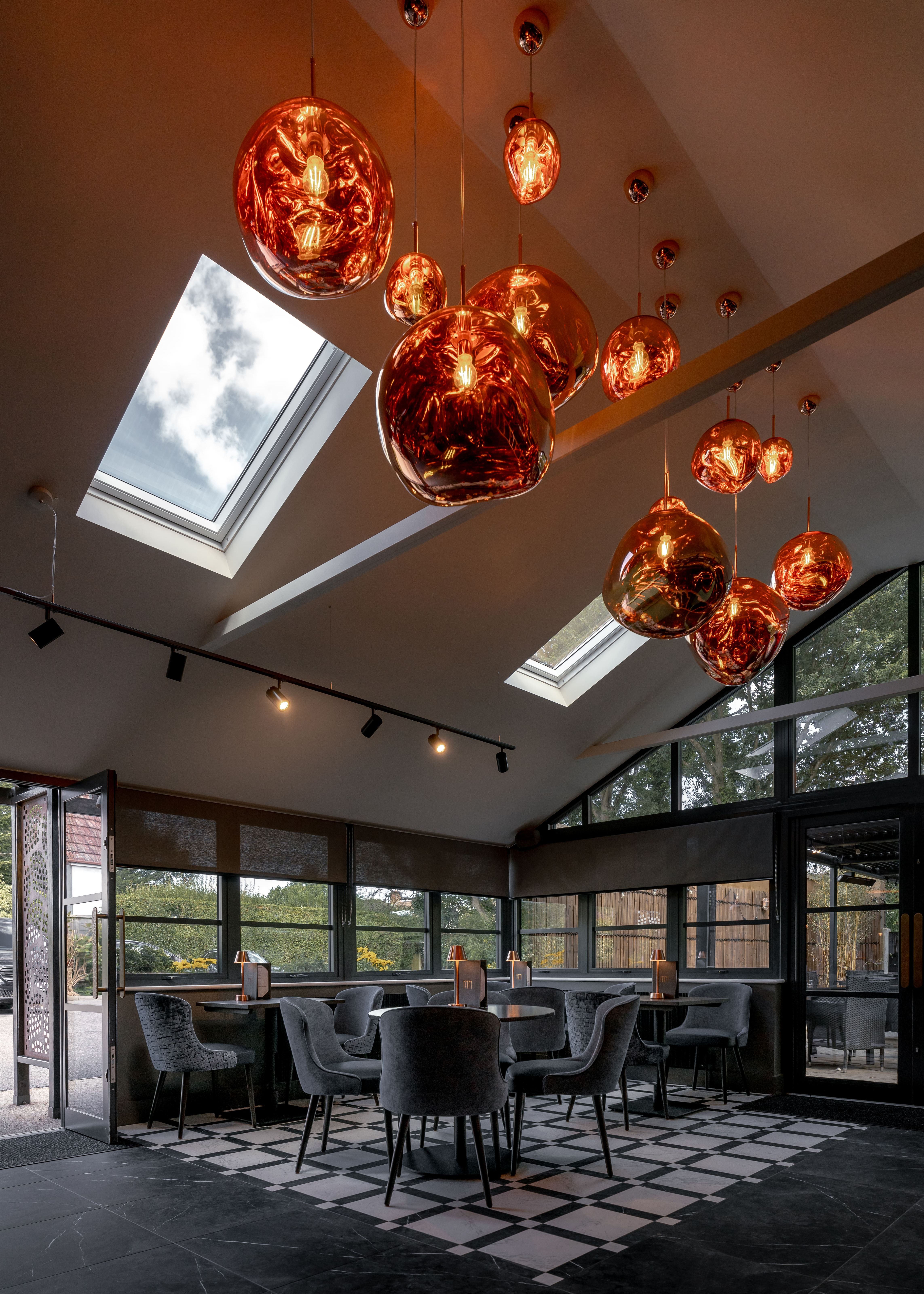 Modern bar area with large skylights, contemporary gray furniture, and sculptural gold pendant lights.