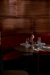 Elegant restaurant booth with red velvet seating, set tableware, and a small golden lamp.
