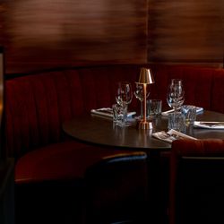 Elegant restaurant booth with red velvet seating, set tableware, and a small golden lamp.
