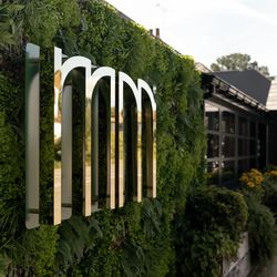 Modern restaurant exterior with gold mirrored sign and lush green wall