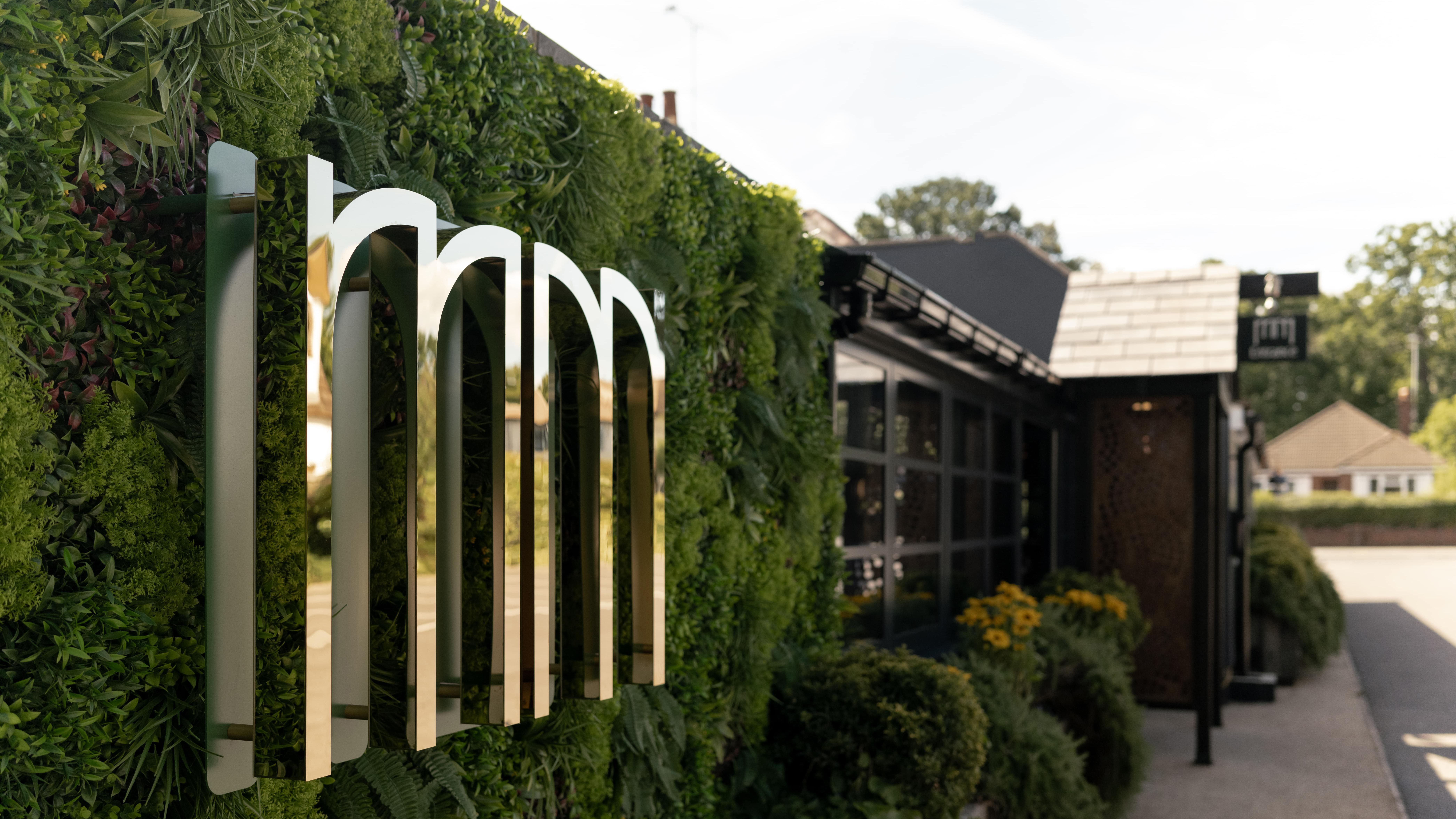 Modern restaurant exterior with gold mirrored sign and lush green wall