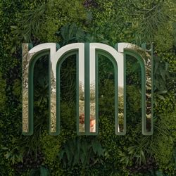Large metallic 'mm' sculpture mounted on a lush green plant wall