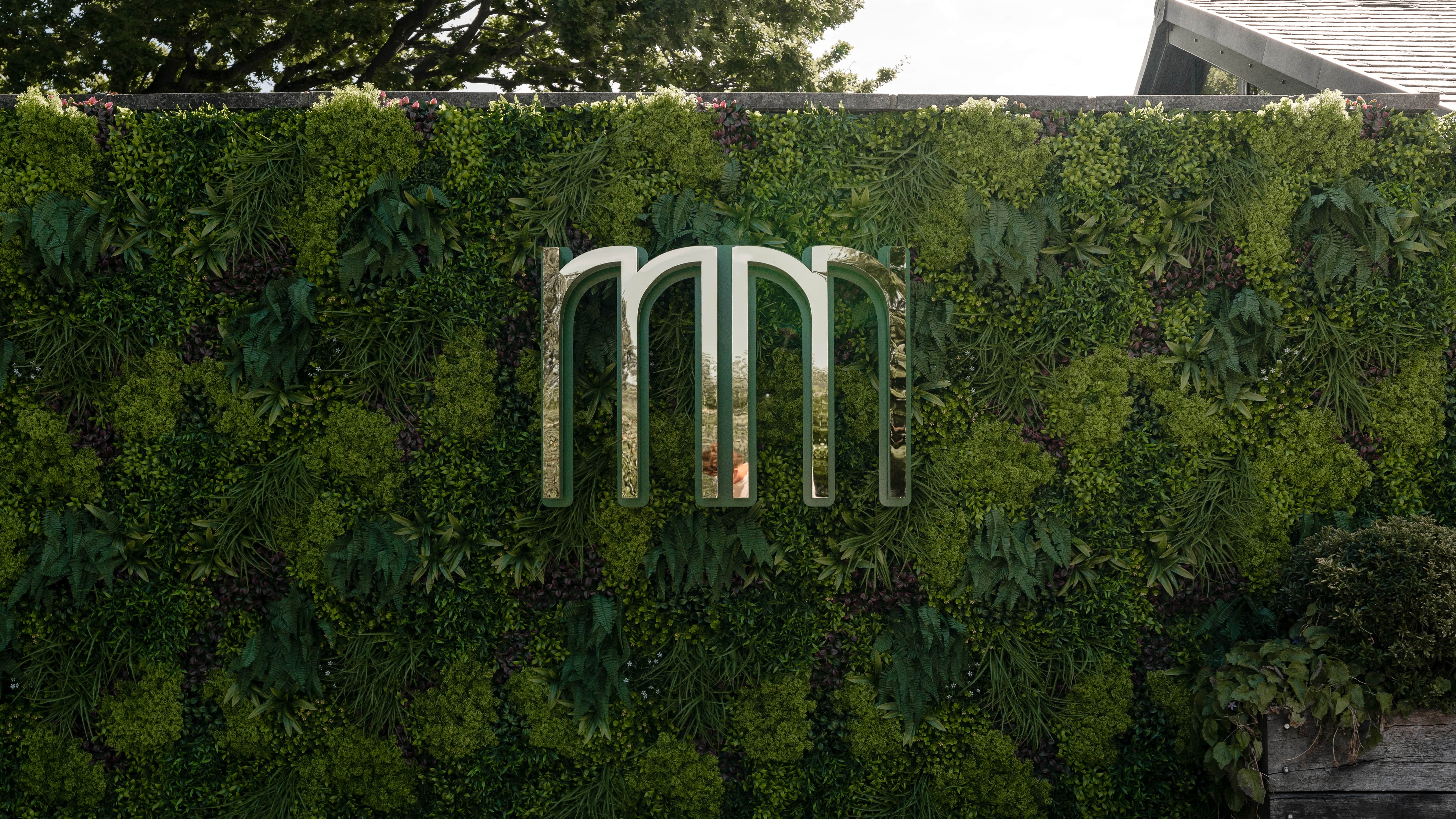 Modern metallic logo on a lush green plant wall outdoors