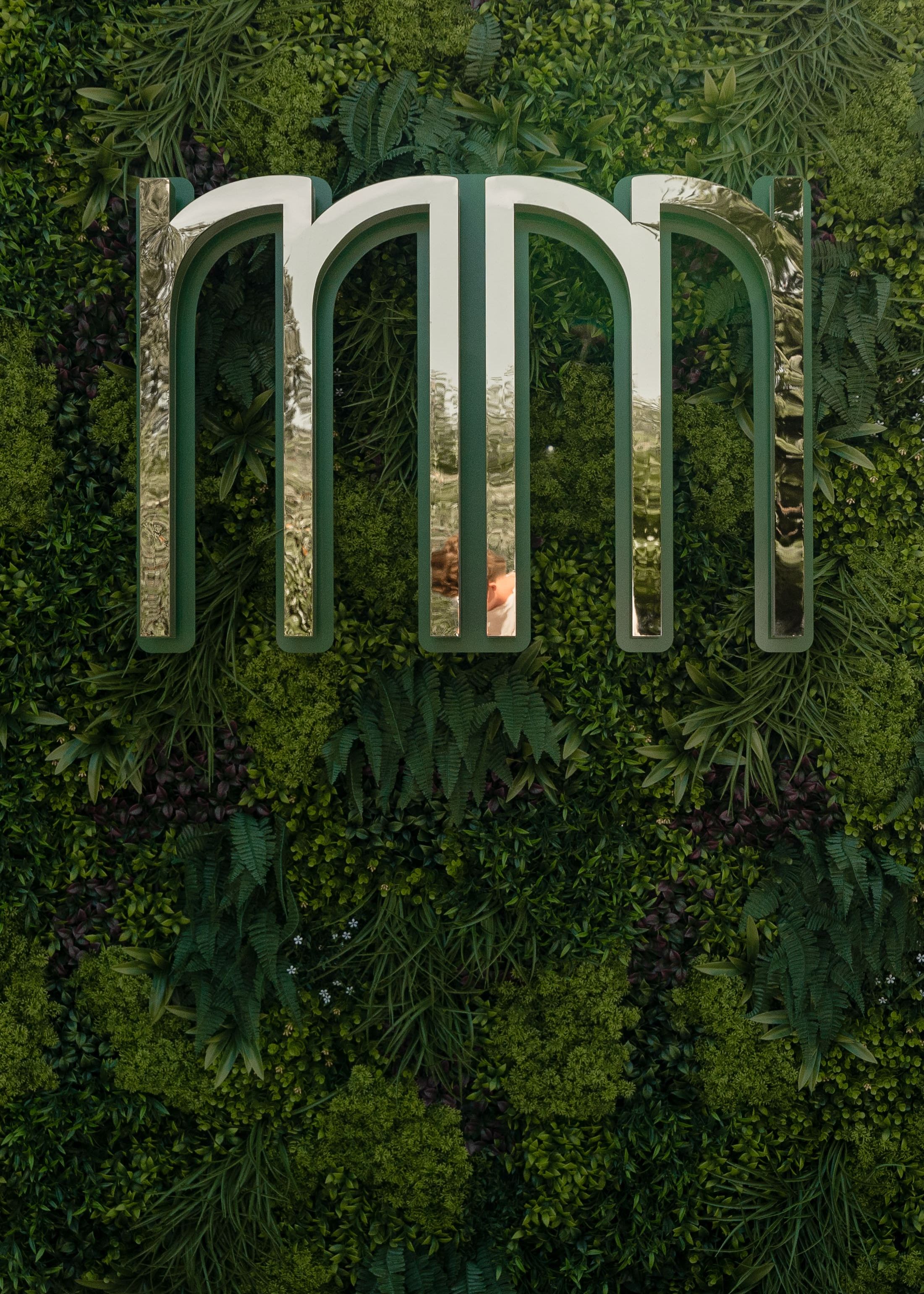 Shiny metallic letters 'mm' mounted on a lush green vertical garden wall.