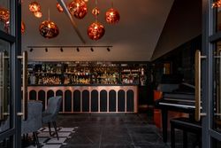 Modern bar area with stylish lighting, velvet chairs, and a piano.