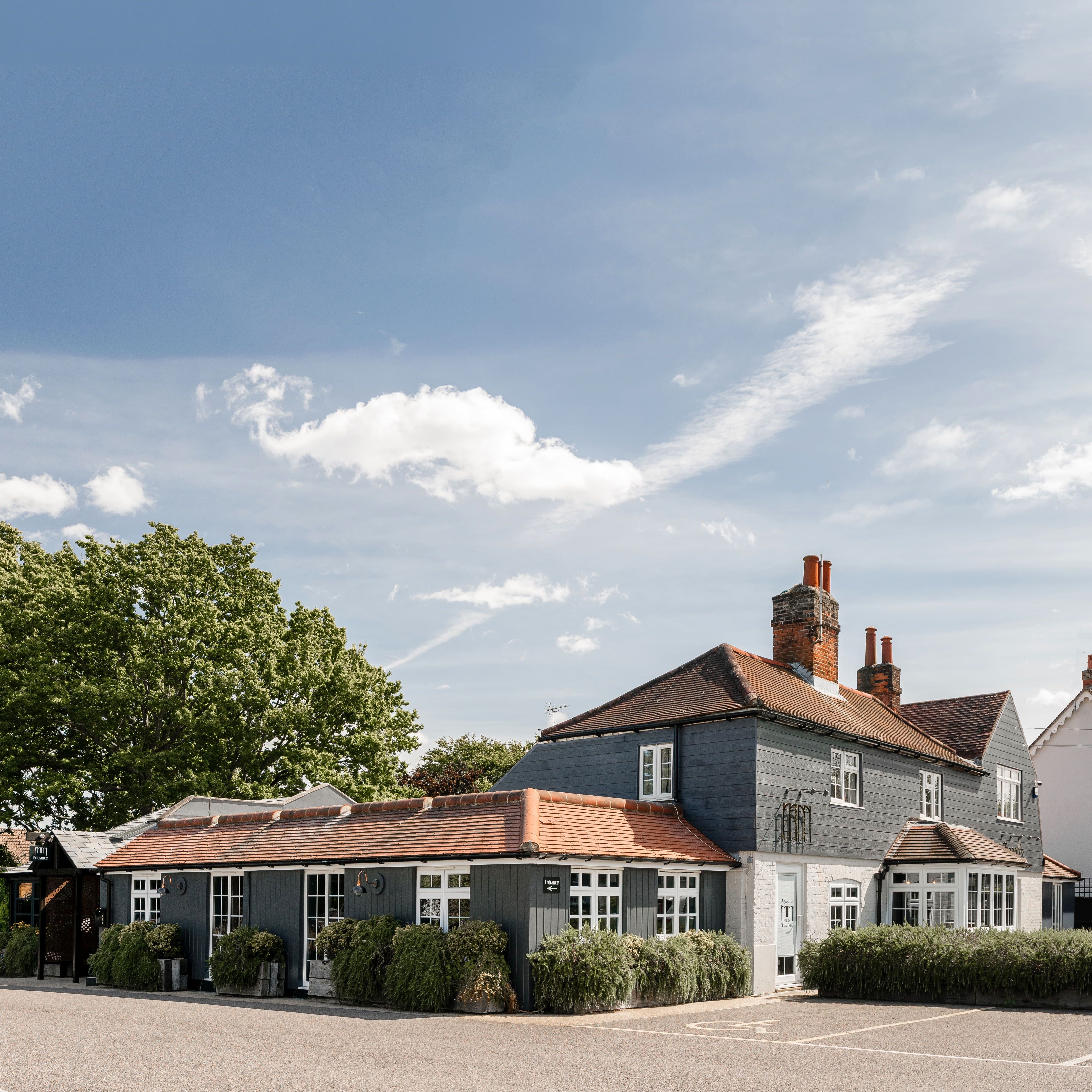 Restaurant with red-tiled roof, white-framed windows, and lush greenery outside on a sunny day.
