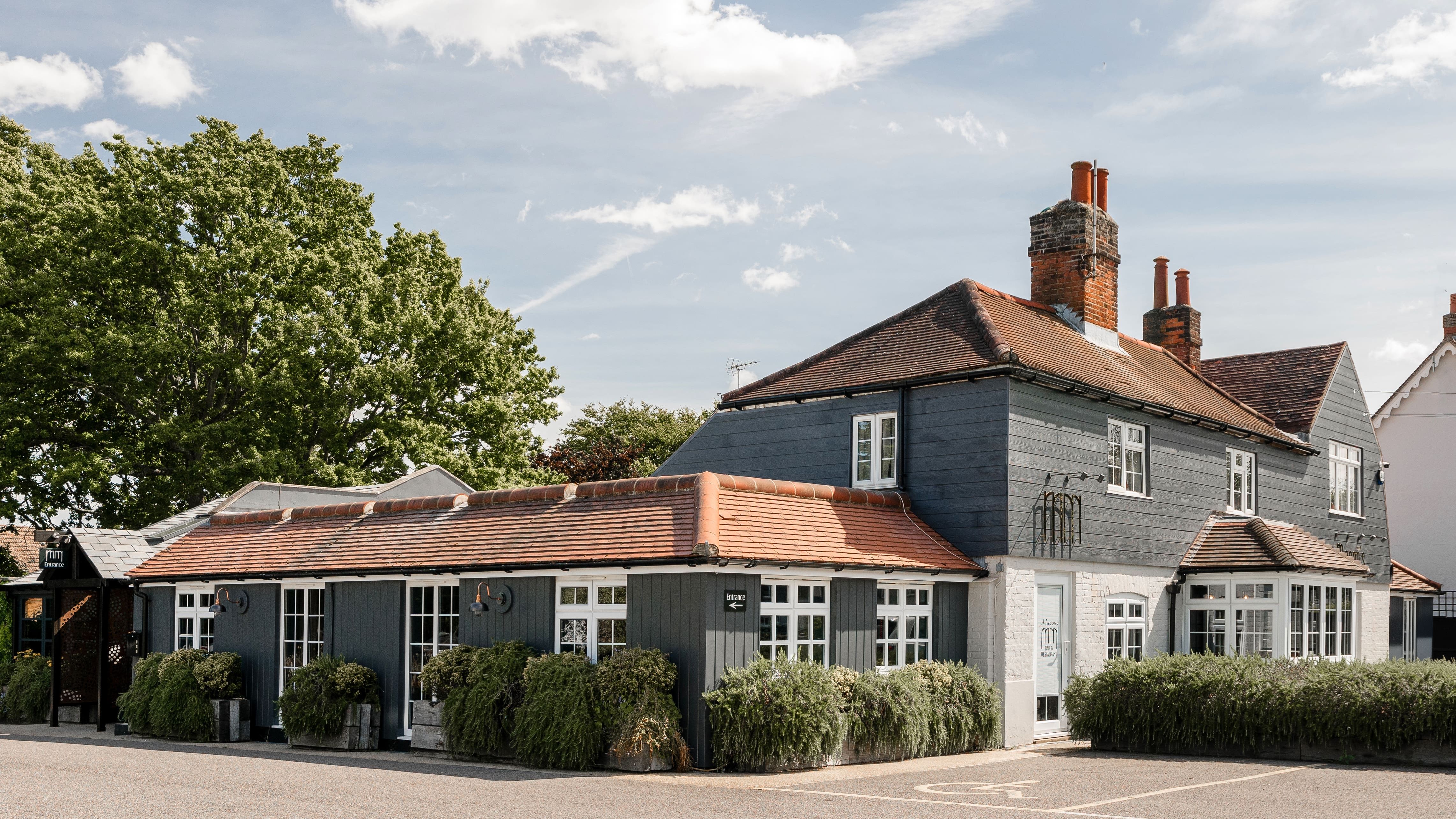 Restaurant with red-tiled roof, white-framed windows, and lush greenery outside on a sunny day.