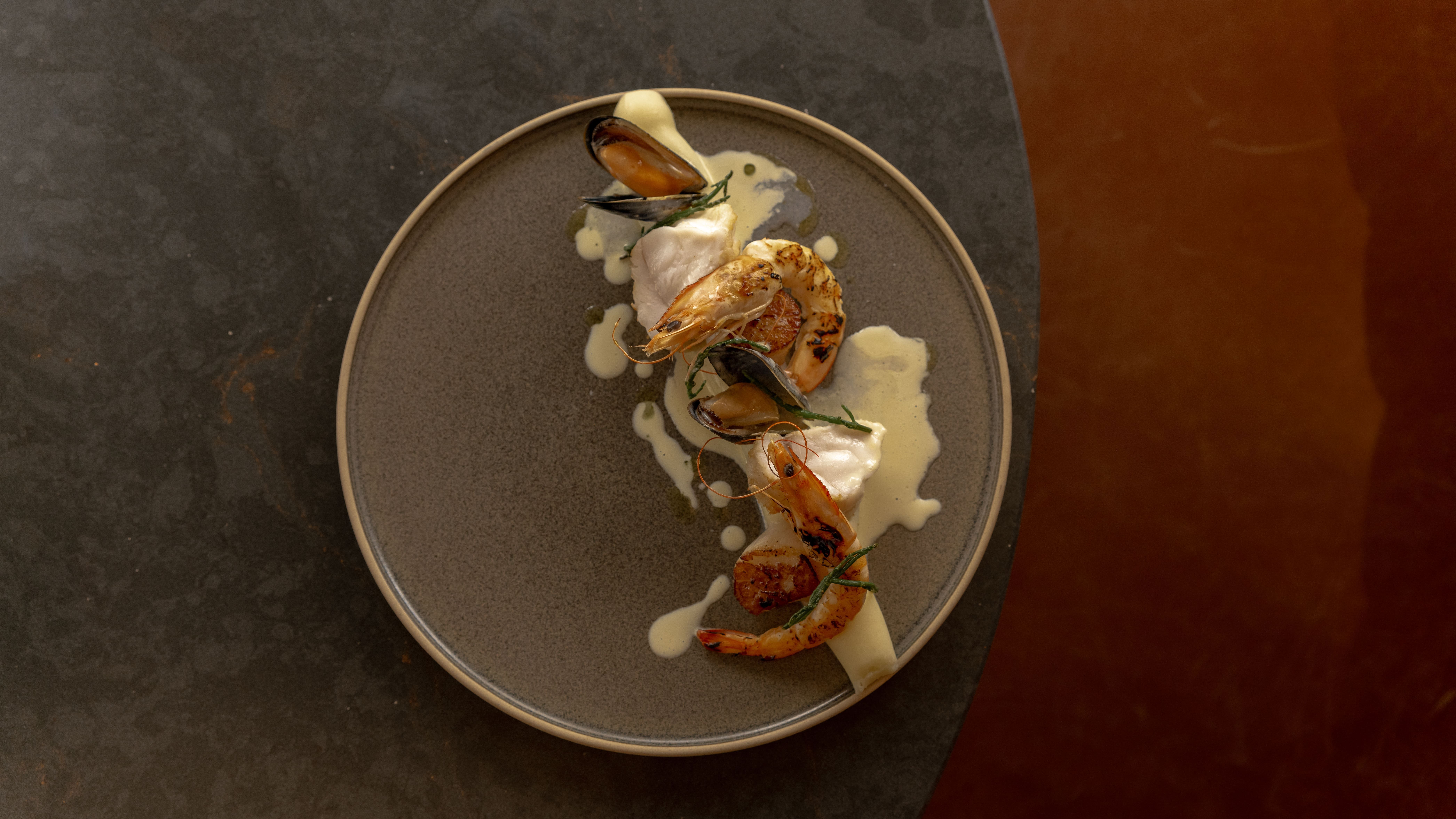 Gourmet seafood dish with prawns, mussels, and creamy sauce on a dark plate