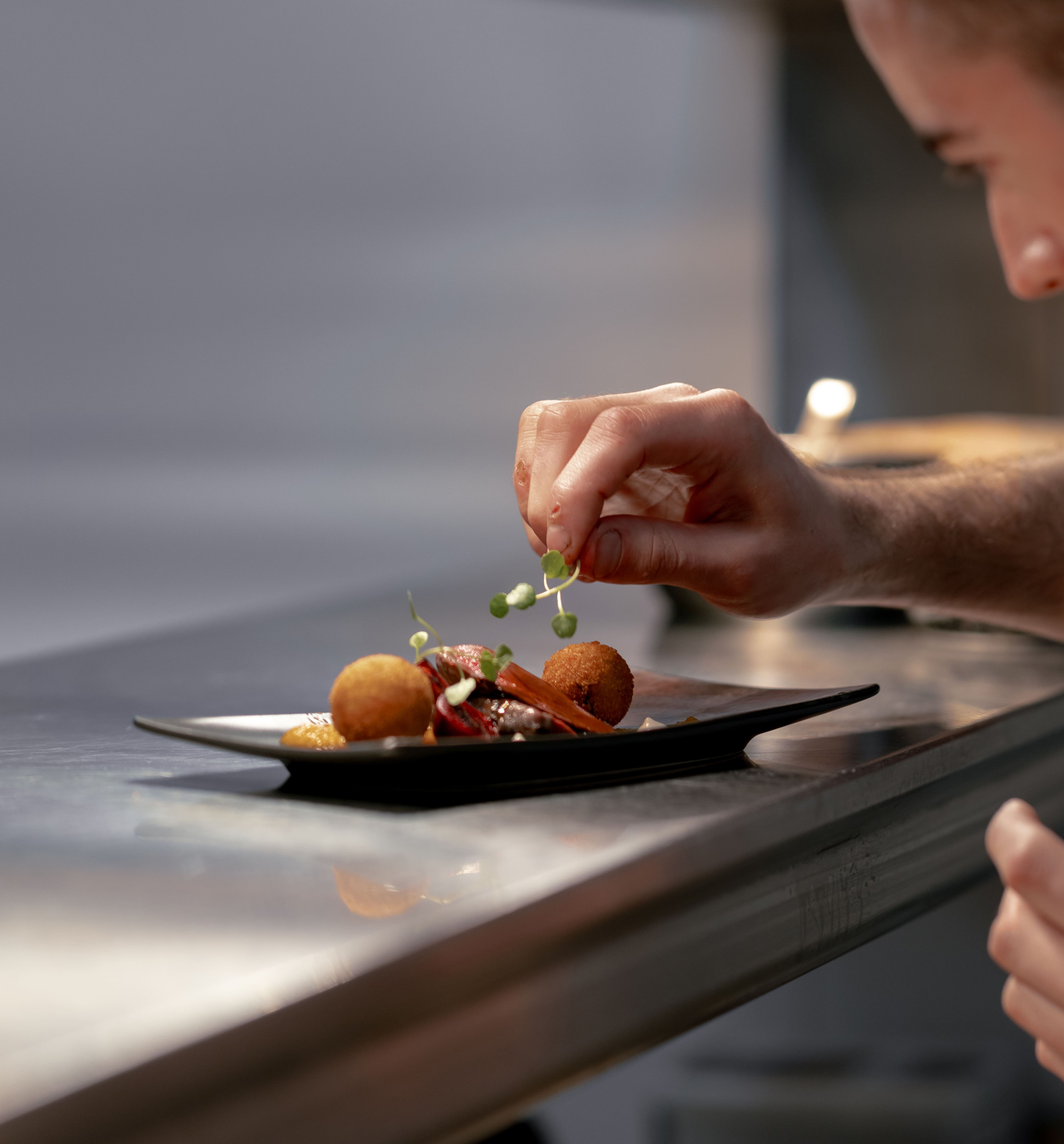 Chef garnishing a plated dish with fresh herbs in a professional kitchen.