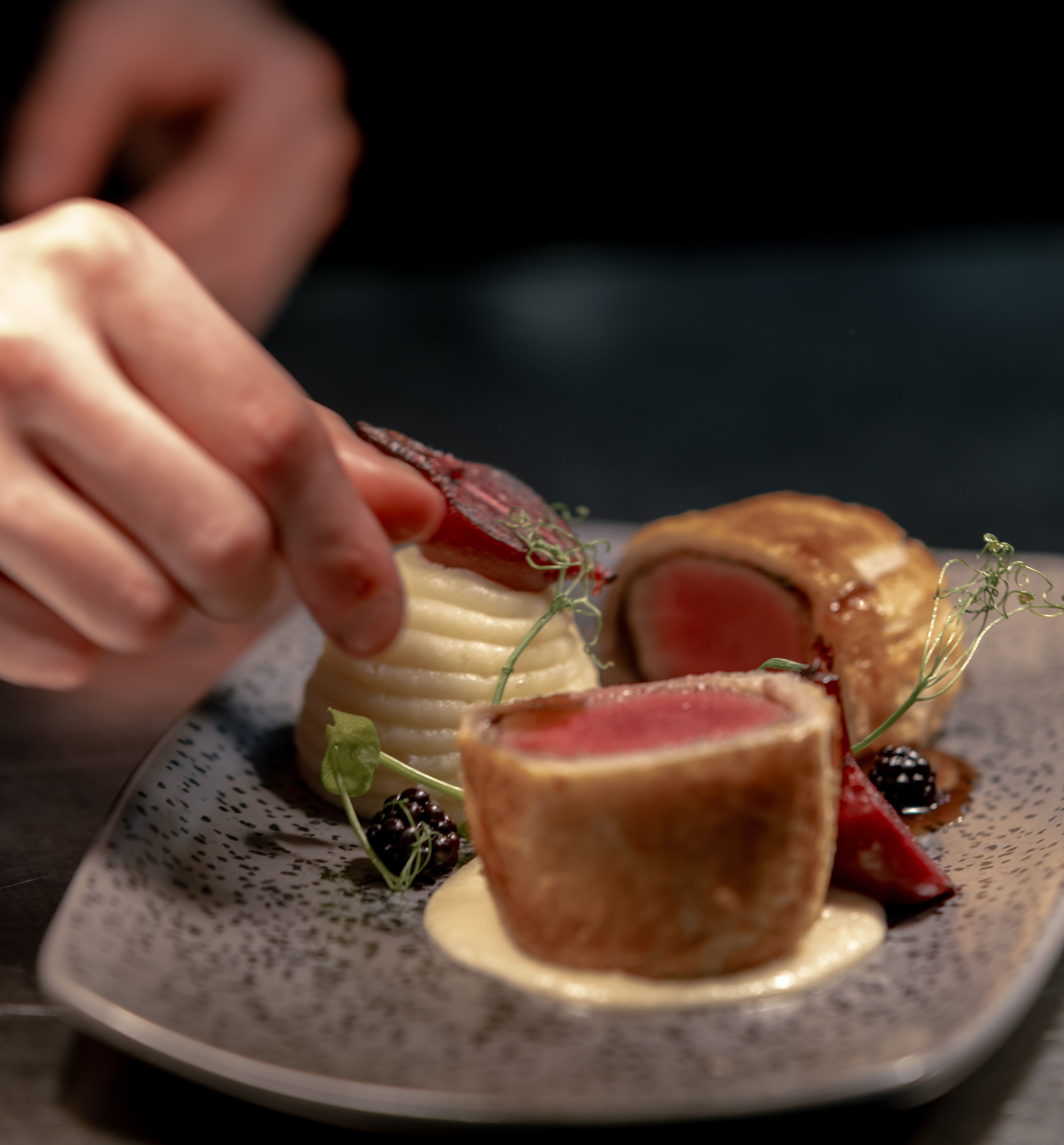 Plated gourmet dish being carefully garnished by a chef's hand