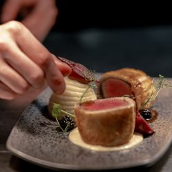 Plated gourmet dish being carefully garnished by a chef's hand
