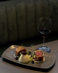 A gourmet plated dish featuring beef Wellington, mashed potatoes, garnishes, and a glass of red wine.
