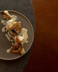 Gourmet seafood dish with shrimp, mussels, and white fish on a gray plate with creamy sauce.