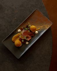 Gourmet plated dish with sliced meat, two golden croquettes, pureed sauce, microgreens, and decorative dollops on a rectangular black plate.