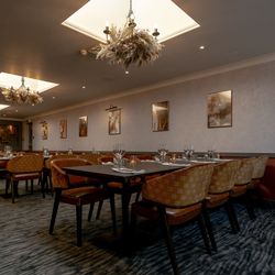 Elegant private dining room with tables set for guests, modern chandeliers, and framed artwork on the walls.