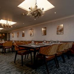 Elegant private dining room with tables set for guests, modern chandeliers, and framed artwork on the walls.