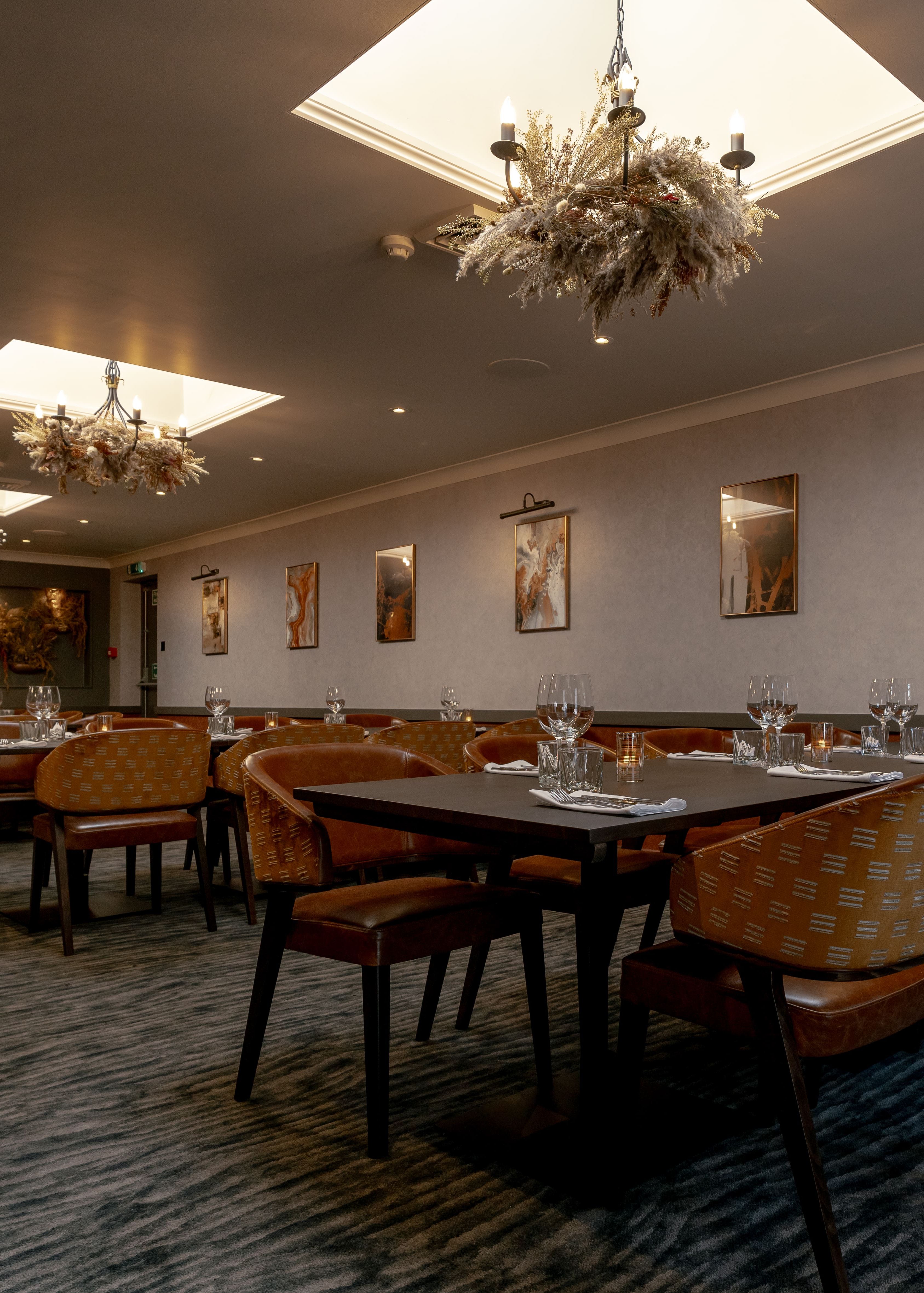 Elegant private dining room with tables set for guests, modern chandeliers, and framed artwork on the walls.