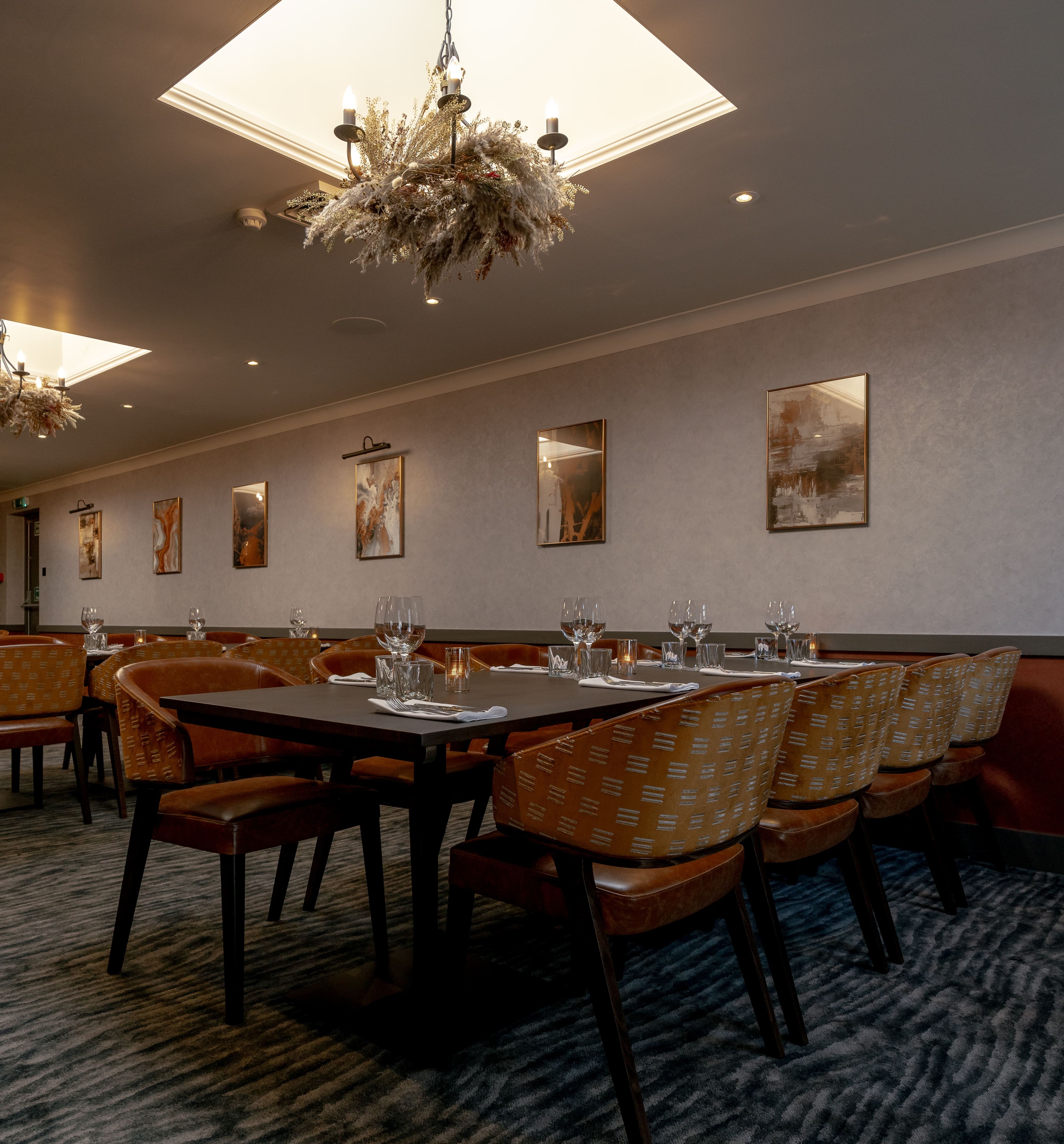 Elegant private dining room with tables set for guests, modern chandeliers, and framed artwork on the walls.
