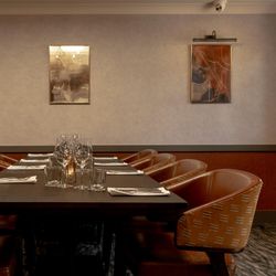 Elegant private dining room with a long table set for a meal, surrounded by brown leather chairs and modern wall art.