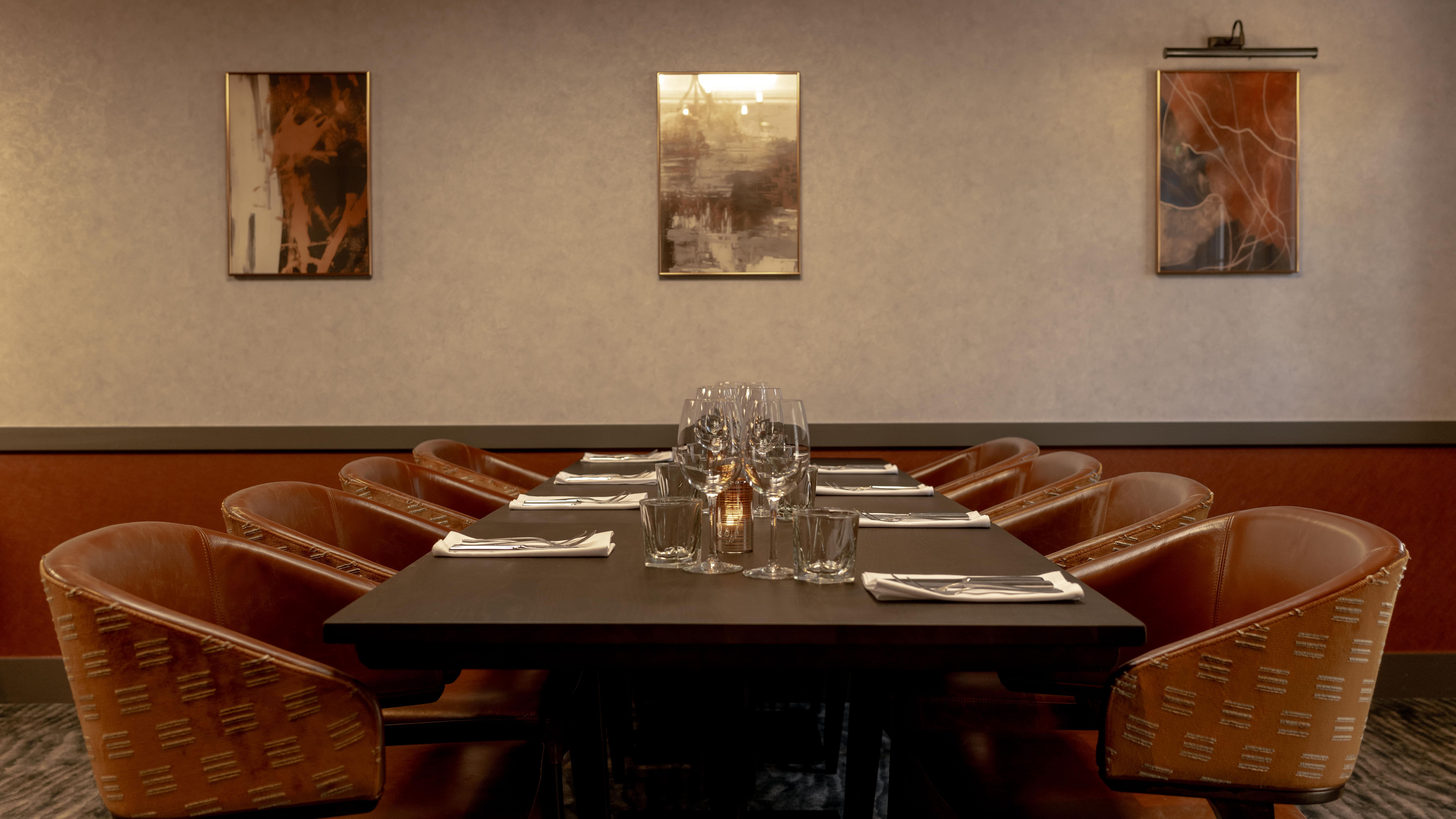 Elegant private dining room with a long table set for a meal, surrounded by brown leather chairs and modern wall art.