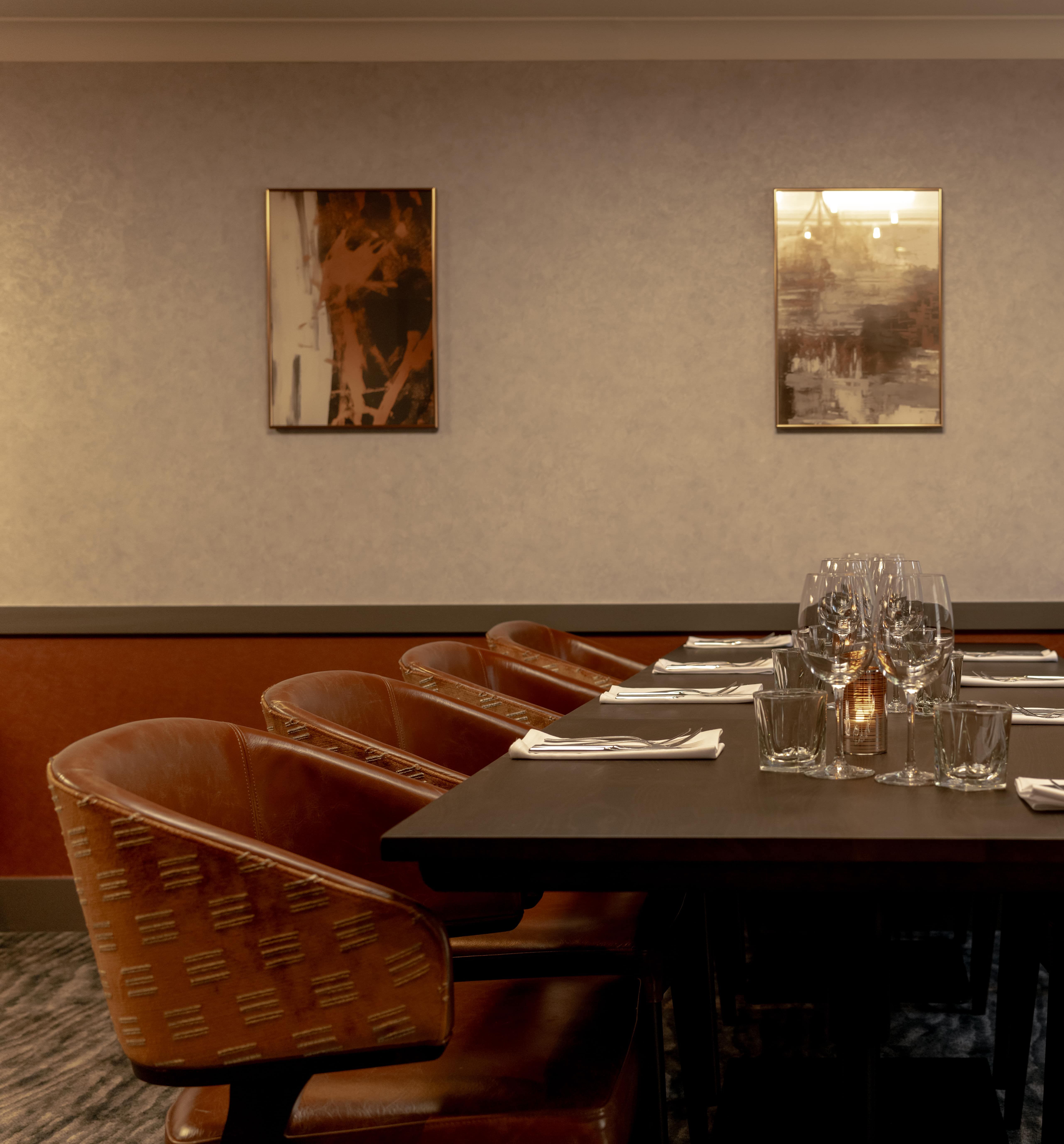 Elegant private dining room with a long table set for a meal, surrounded by brown leather chairs and modern wall art.