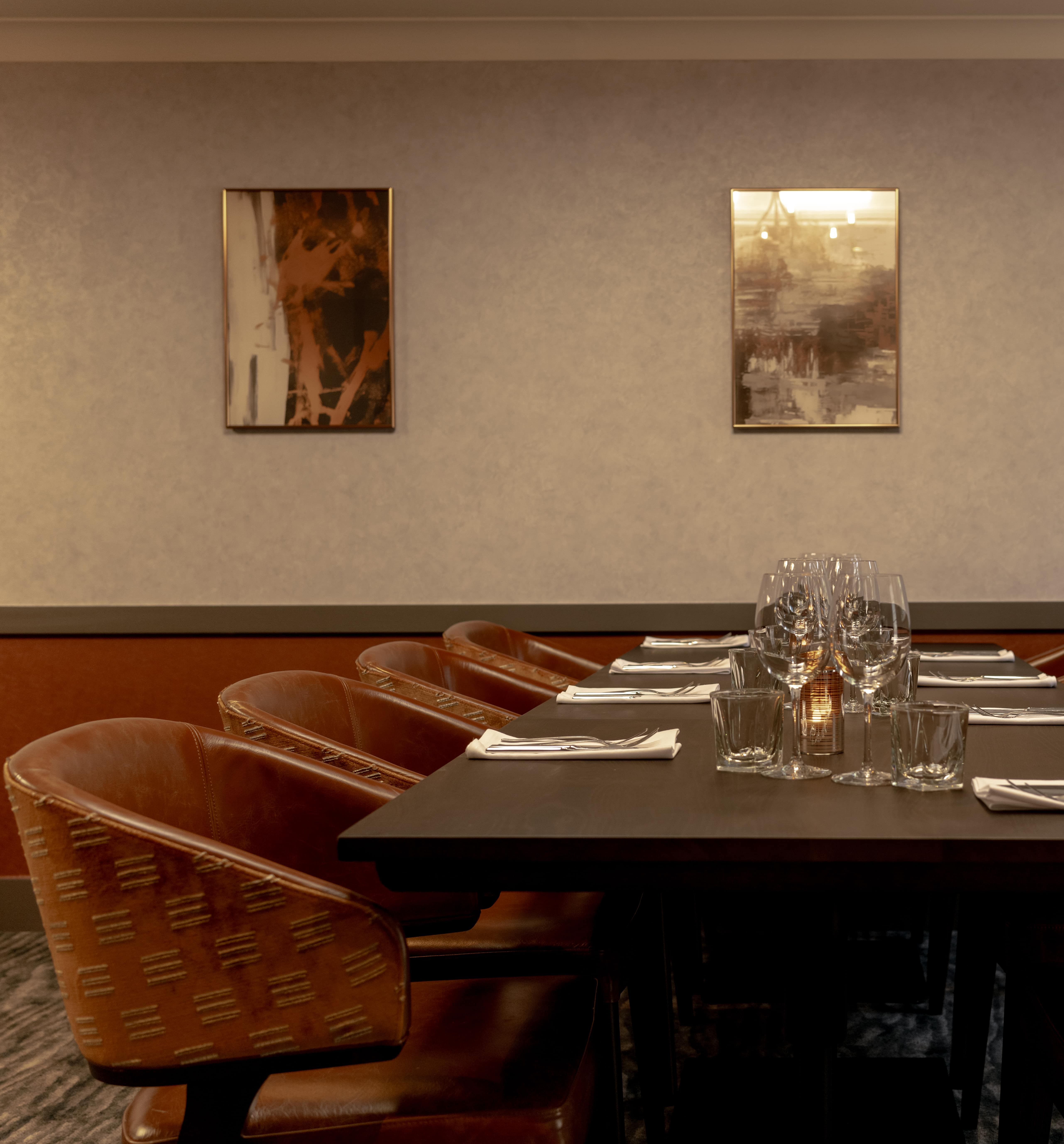 Elegant private dining room with a long table set for a meal, surrounded by brown leather chairs and modern wall art.