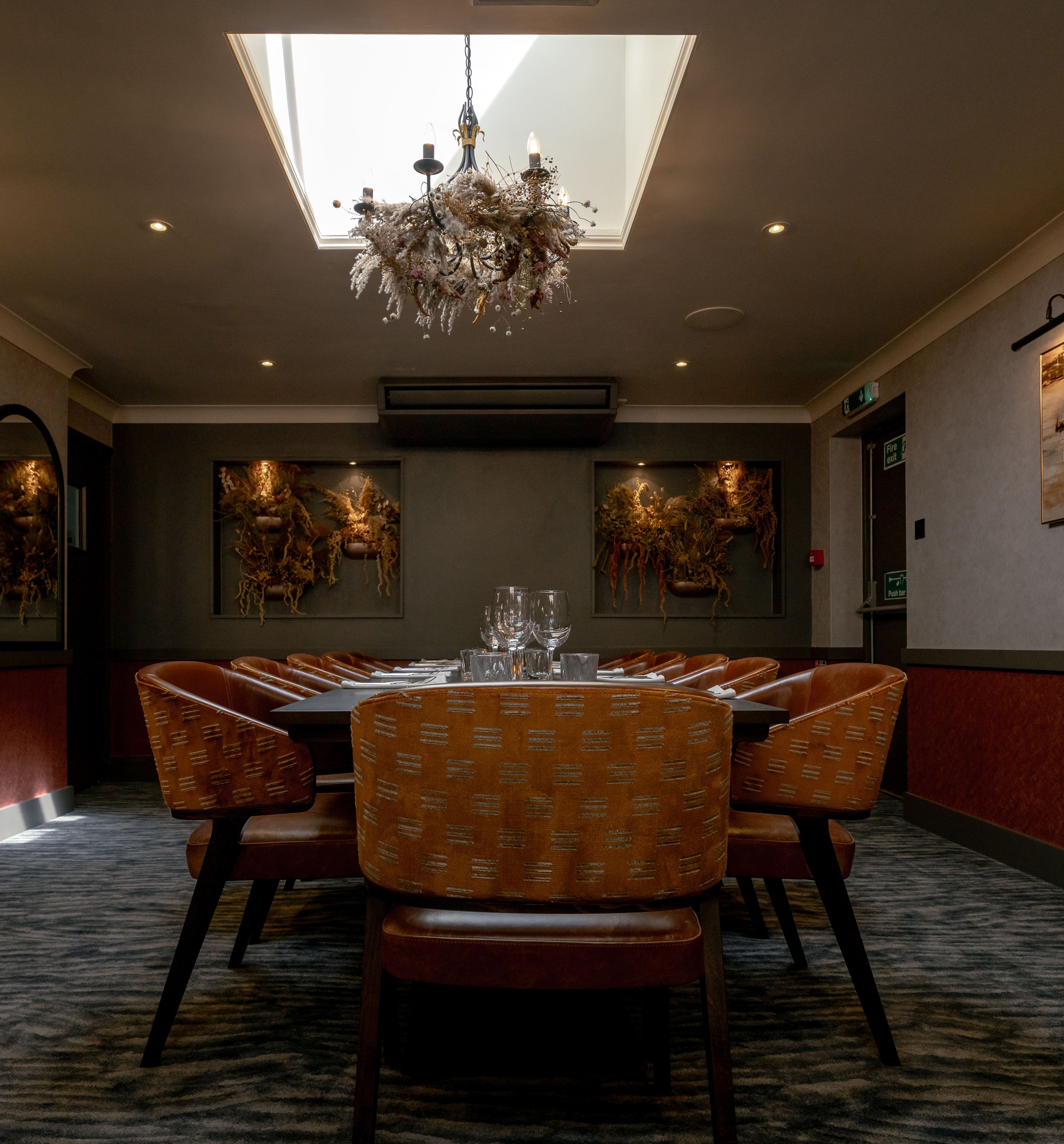 Elegant private dining room with orange chairs, large table, chandelier, and artwork on the walls.