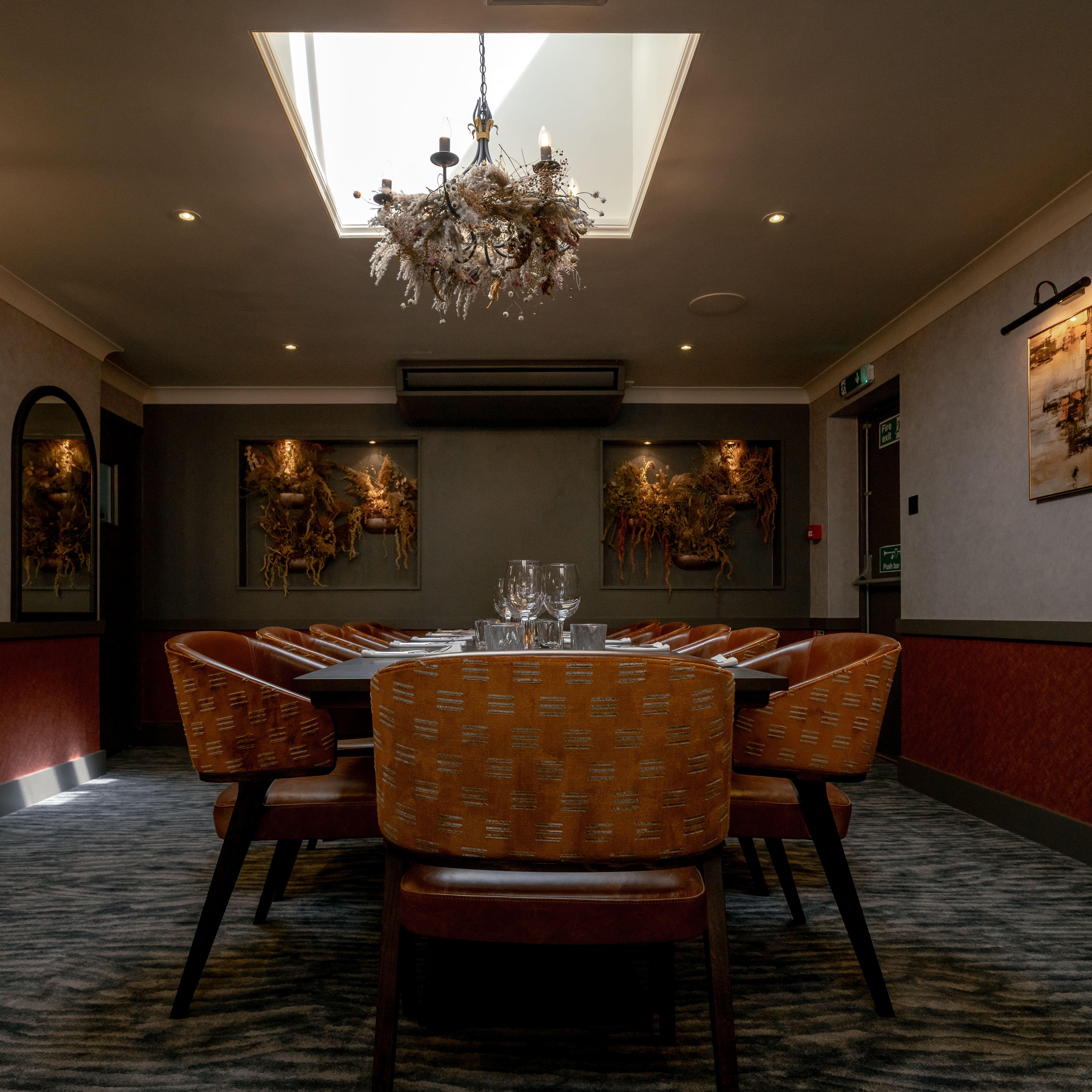Elegant private dining room with orange chairs, large table, chandelier, and artwork on the walls.