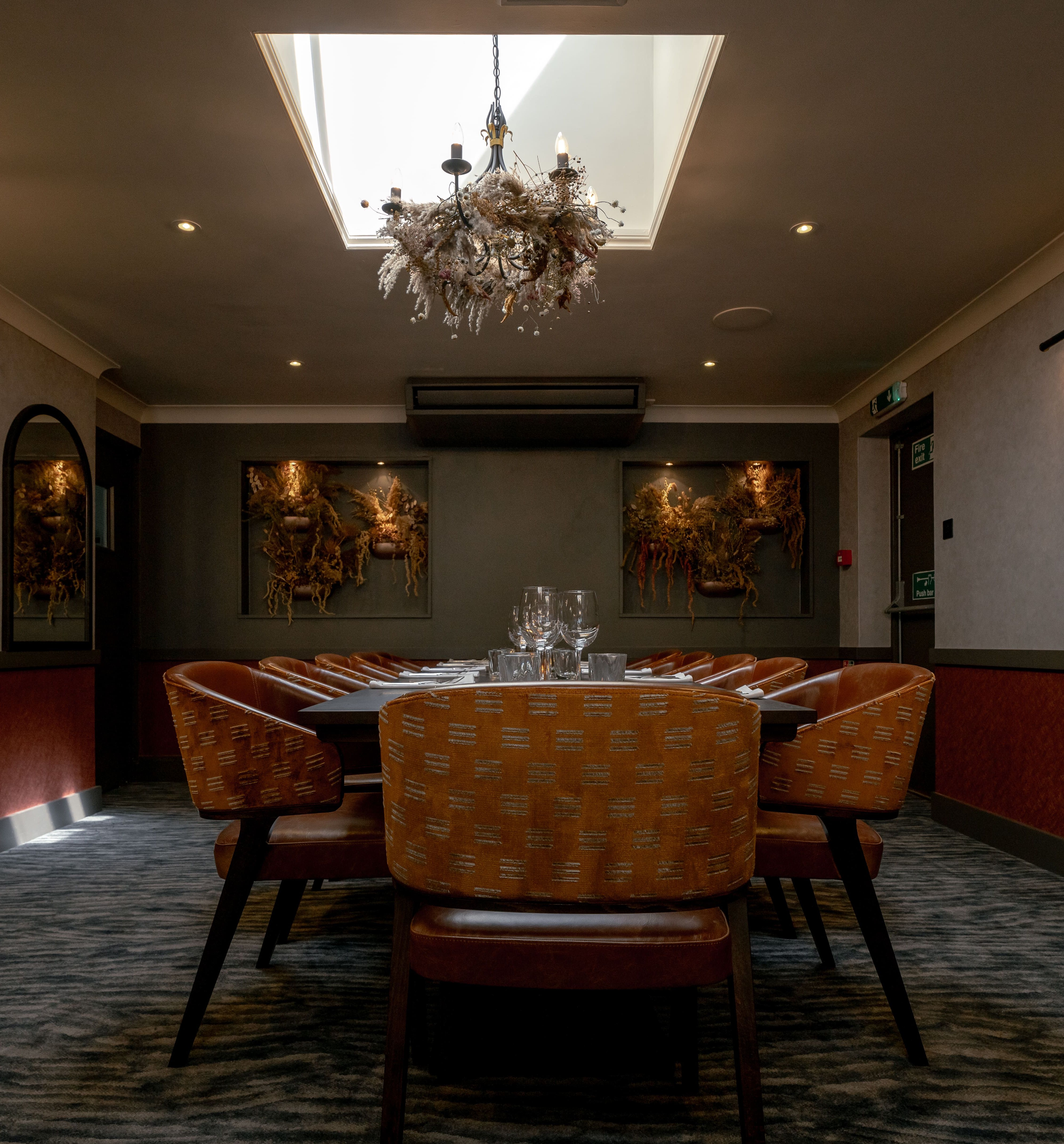 Elegant private dining room with orange chairs, large table, chandelier, and artwork on the walls.