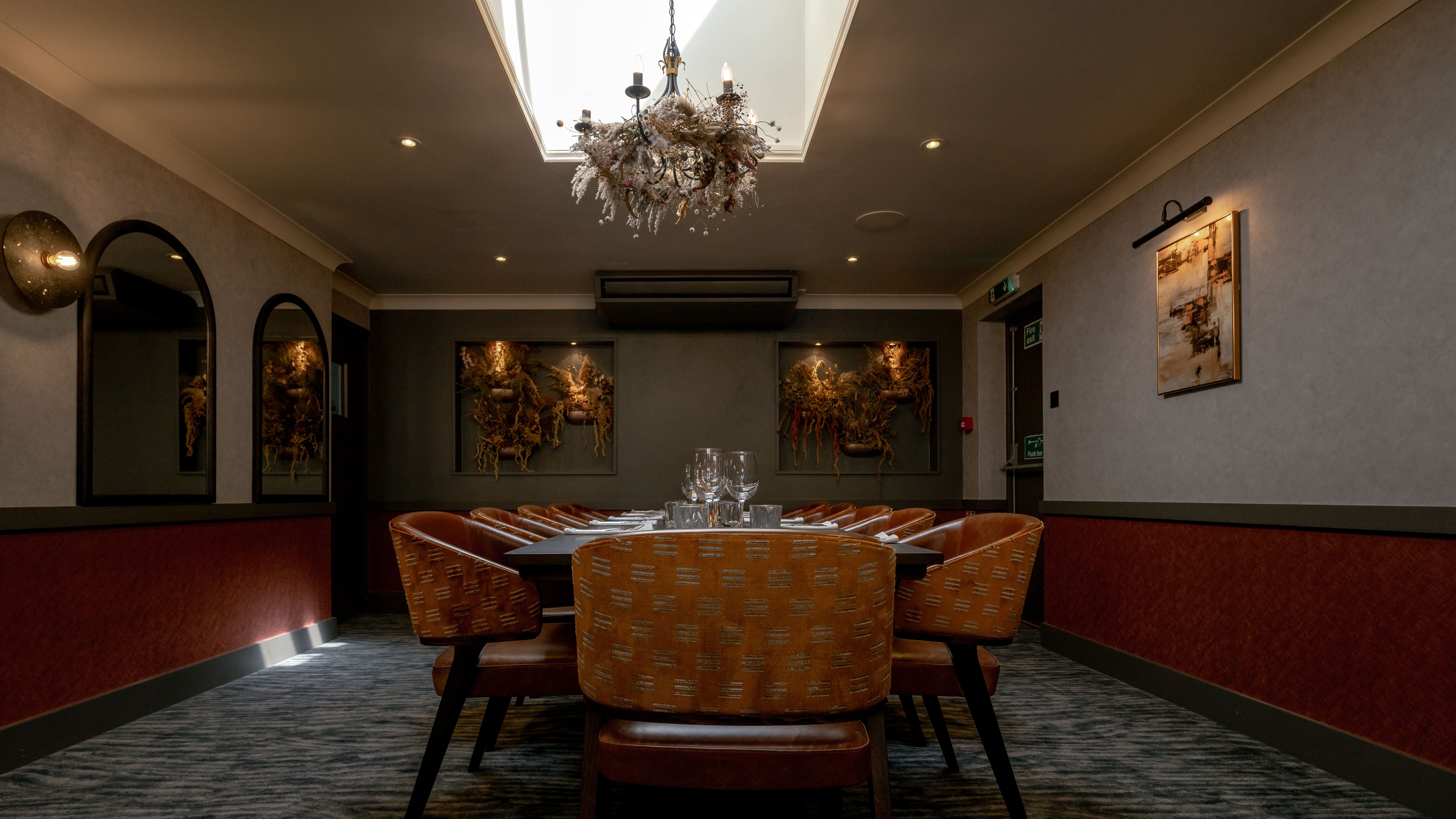 Elegant private dining room with orange chairs, large table, chandelier, and artwork on the walls.