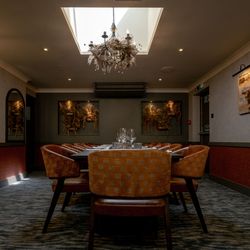 Elegant private dining room with orange chairs, large table, chandelier, and artwork on the walls.