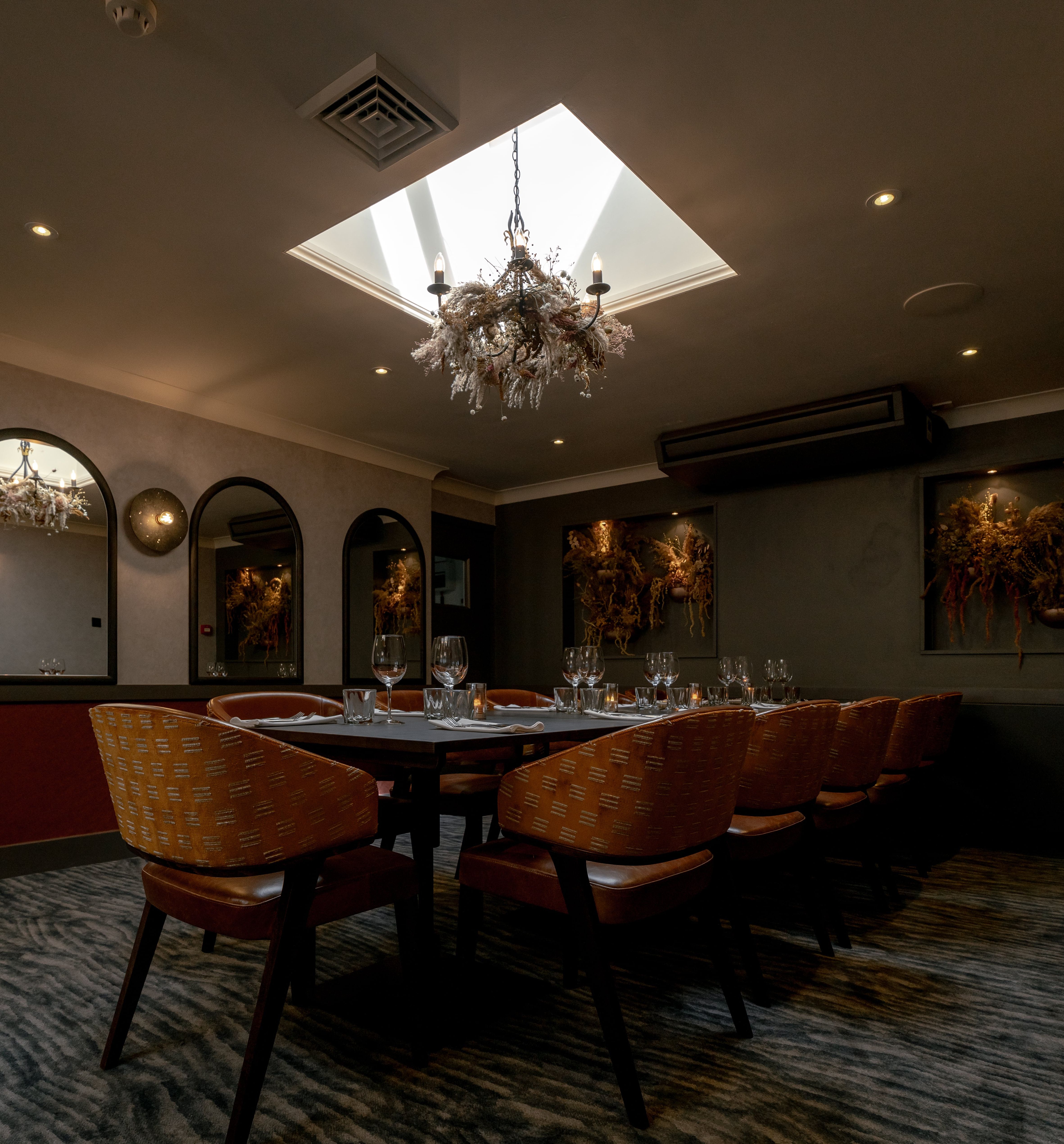 Elegant private dining room with a set table, modern decor, and chandelier lighting under a skylight.