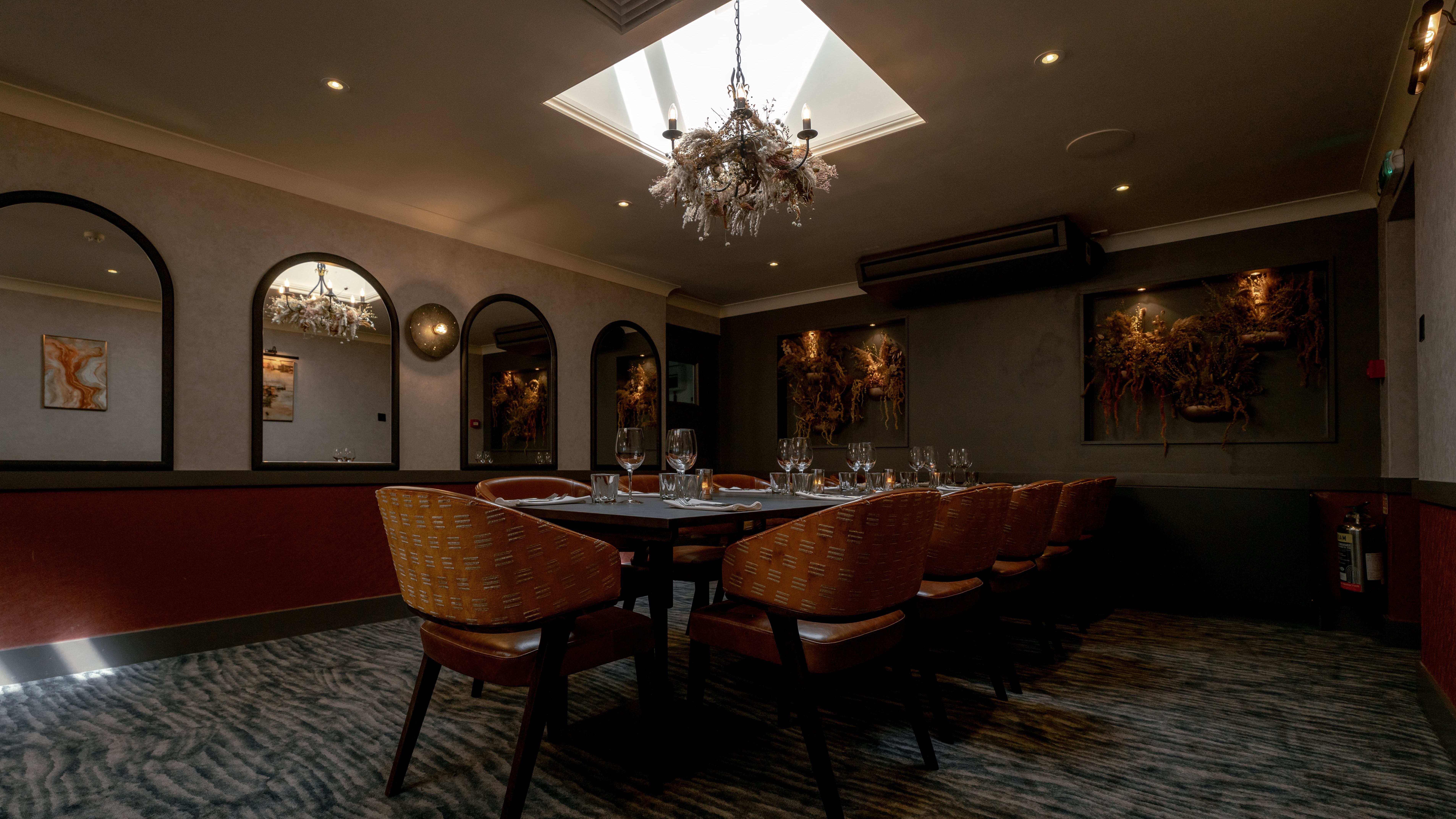 Elegant private dining room with a set table, modern decor, and chandelier lighting under a skylight.
