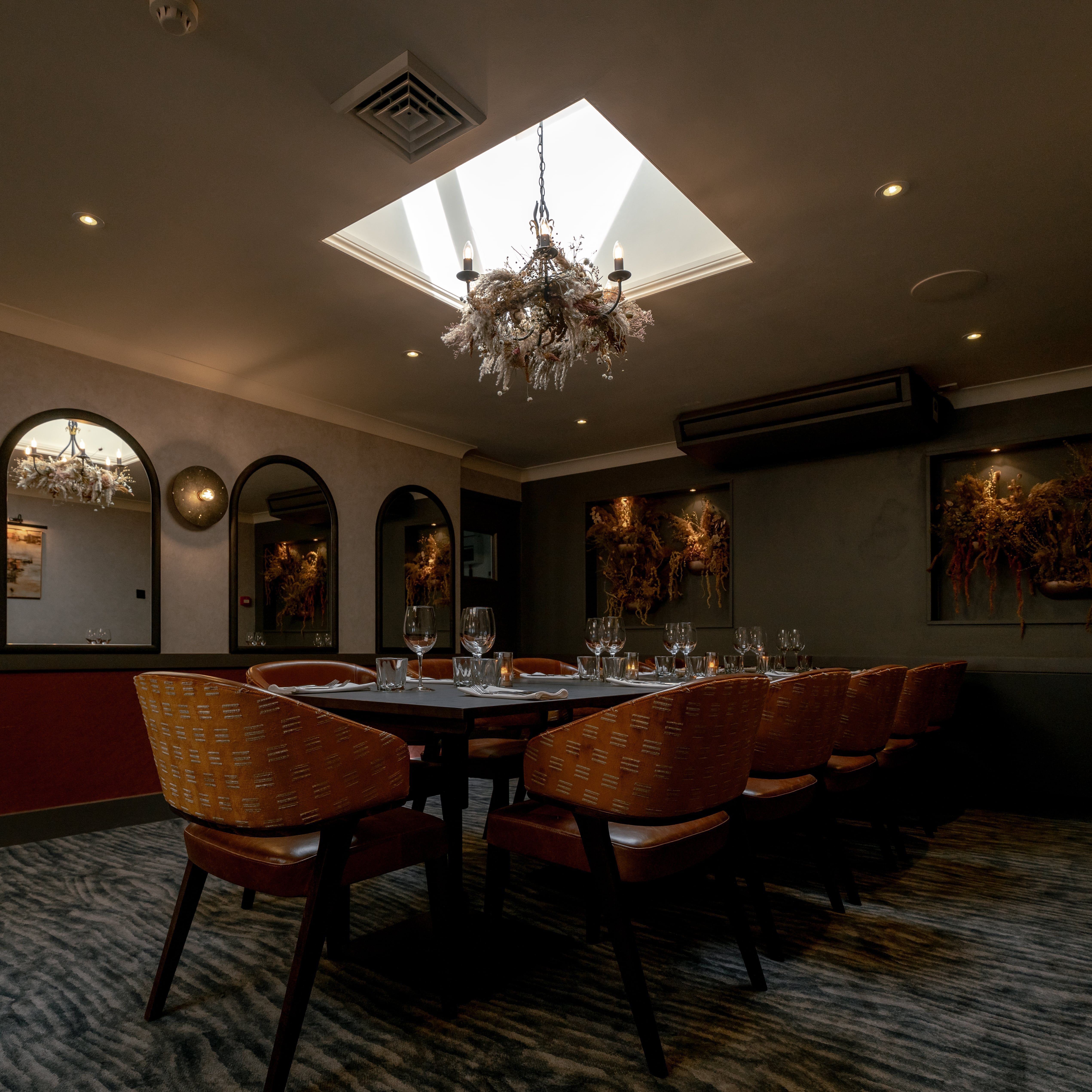 Elegant private dining room with a set table, modern decor, and chandelier lighting under a skylight.