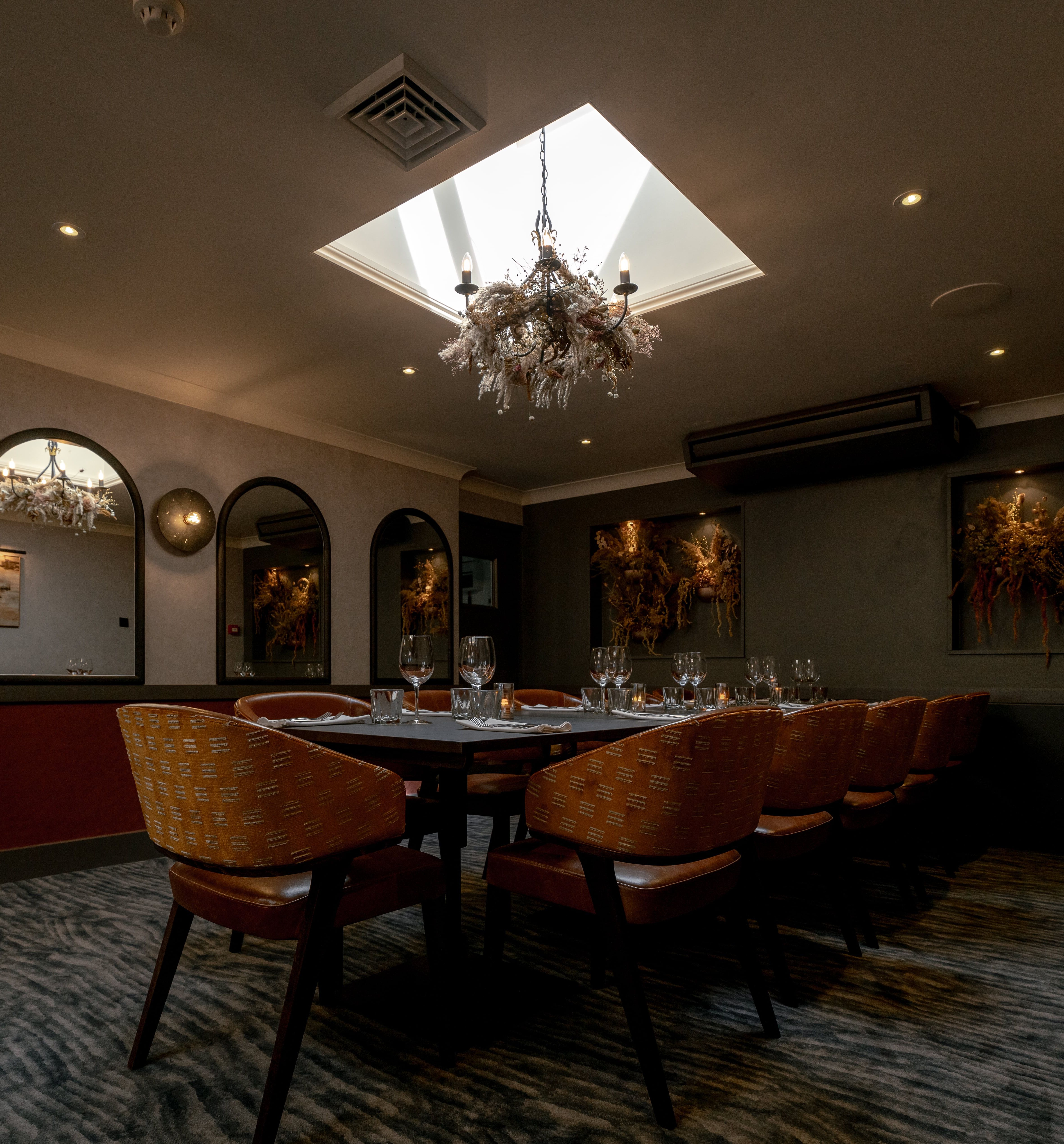 Elegant private dining room with a set table, modern decor, and chandelier lighting under a skylight.