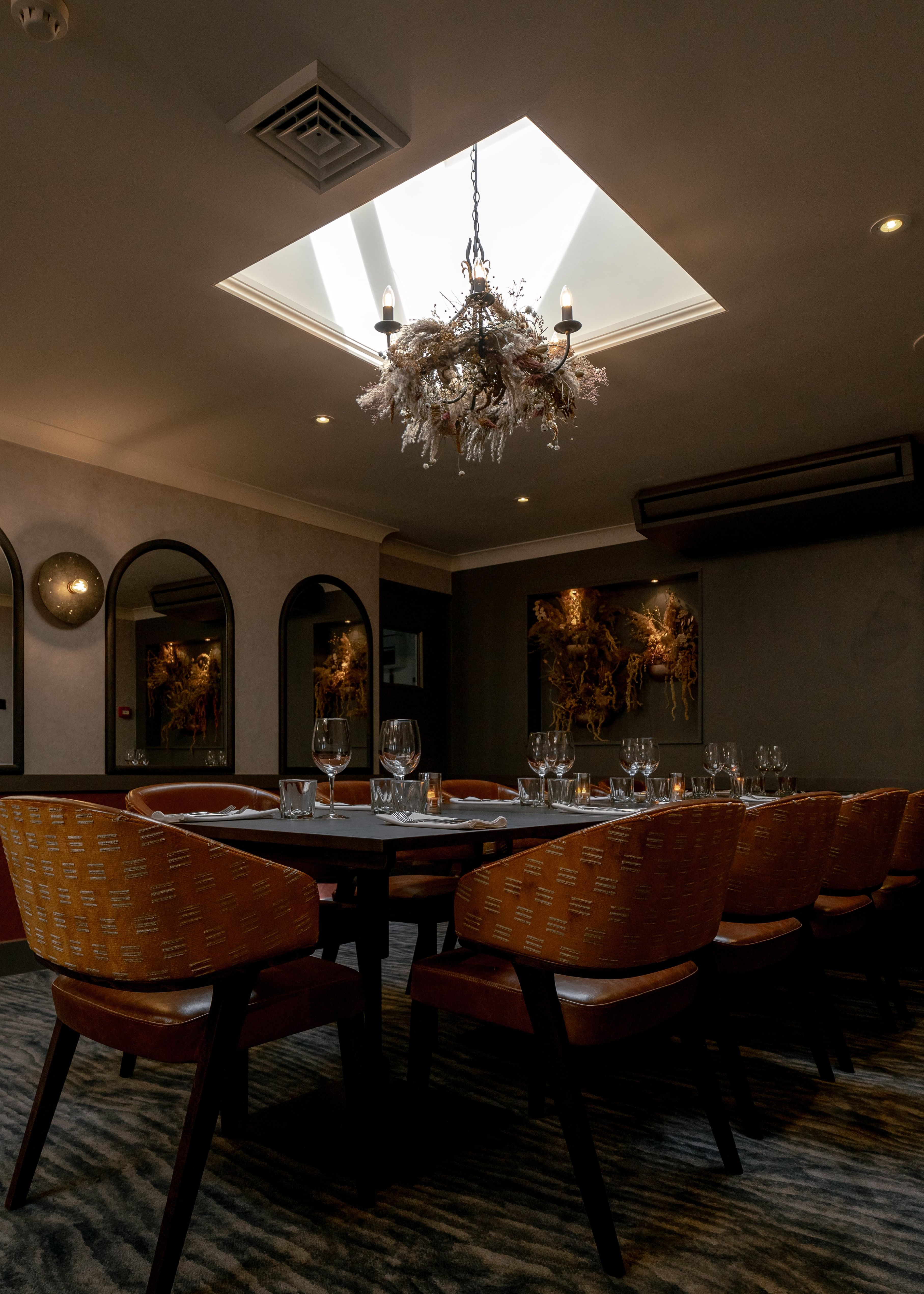 Elegant private dining room with a set table, modern decor, and chandelier lighting under a skylight.