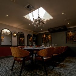 Elegant private dining room with a set table, modern decor, and chandelier lighting under a skylight.