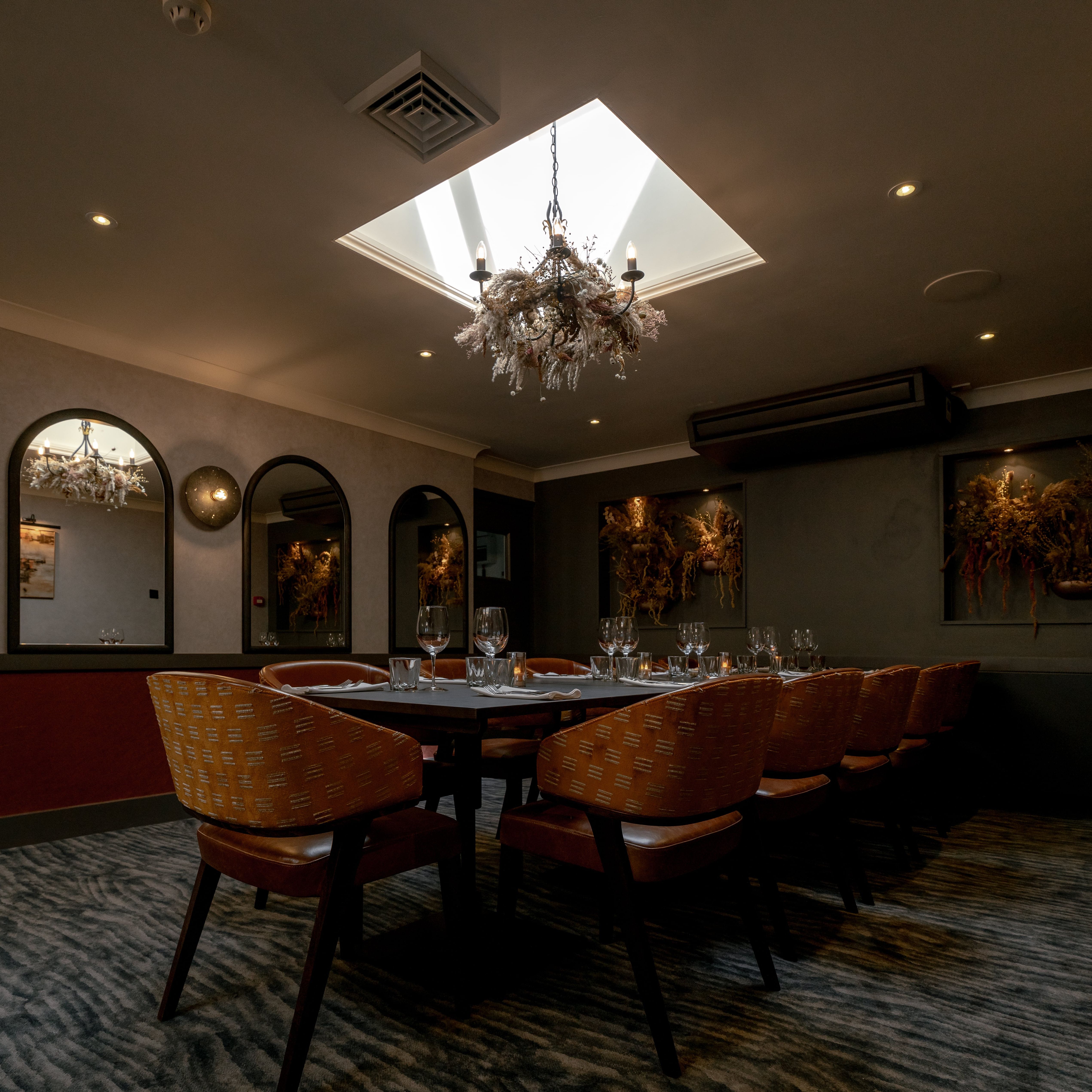 Elegant private dining room with a set table, modern decor, and chandelier lighting under a skylight.