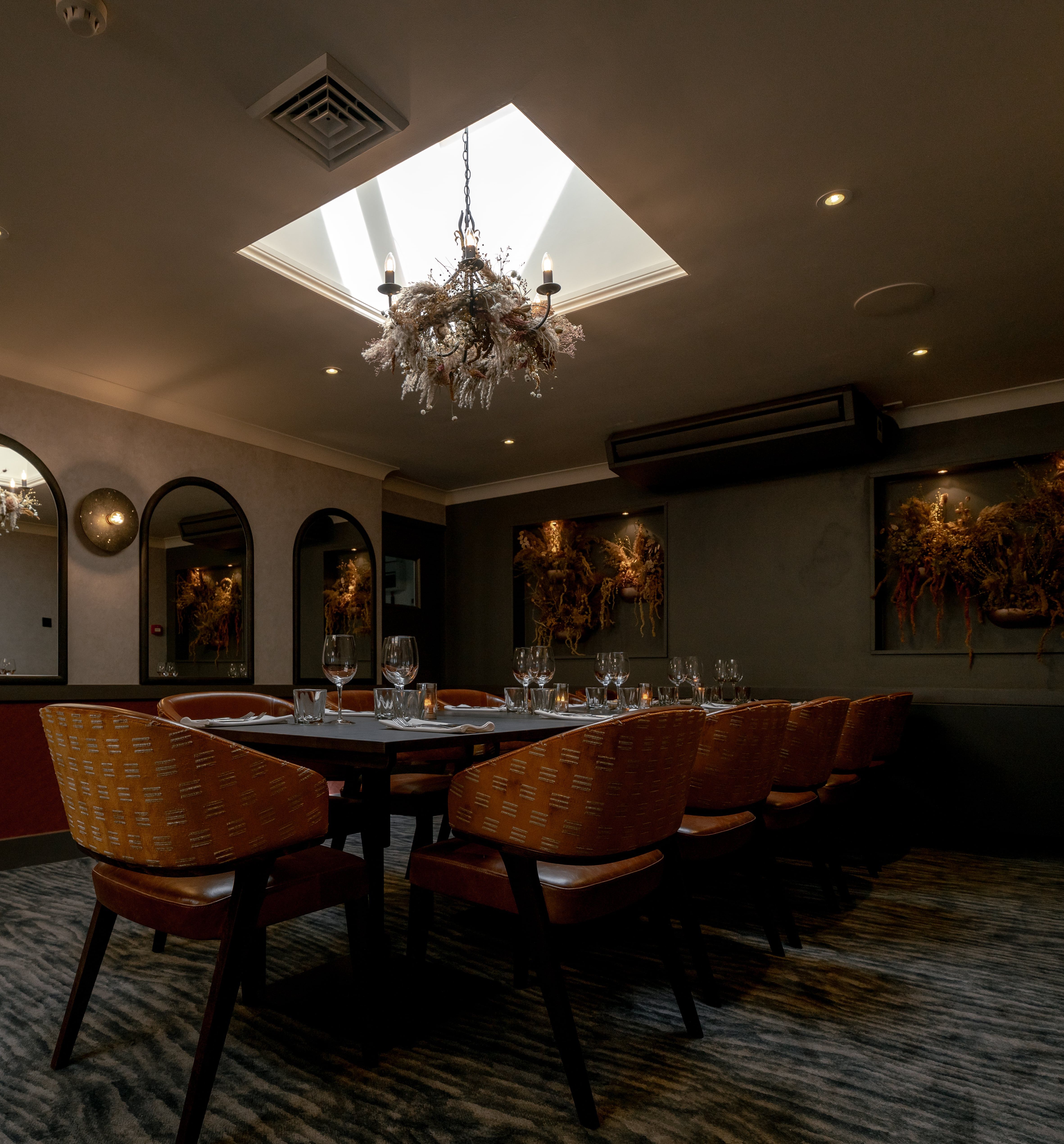 Elegant private dining room with a set table, modern decor, and chandelier lighting under a skylight.