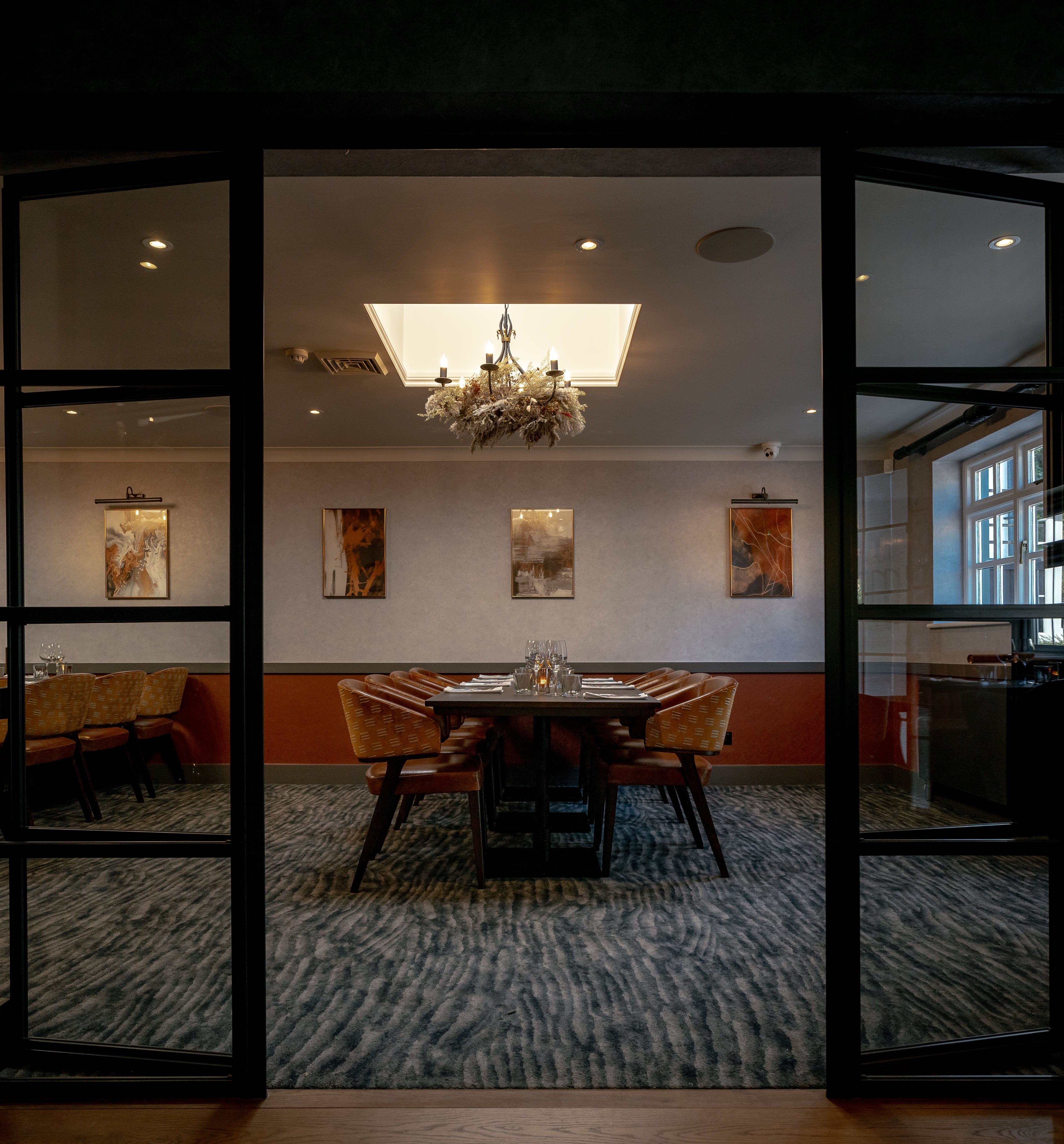 Elegant private dining room with modern decor and a chandelier, featuring a large table surrounded by chairs.