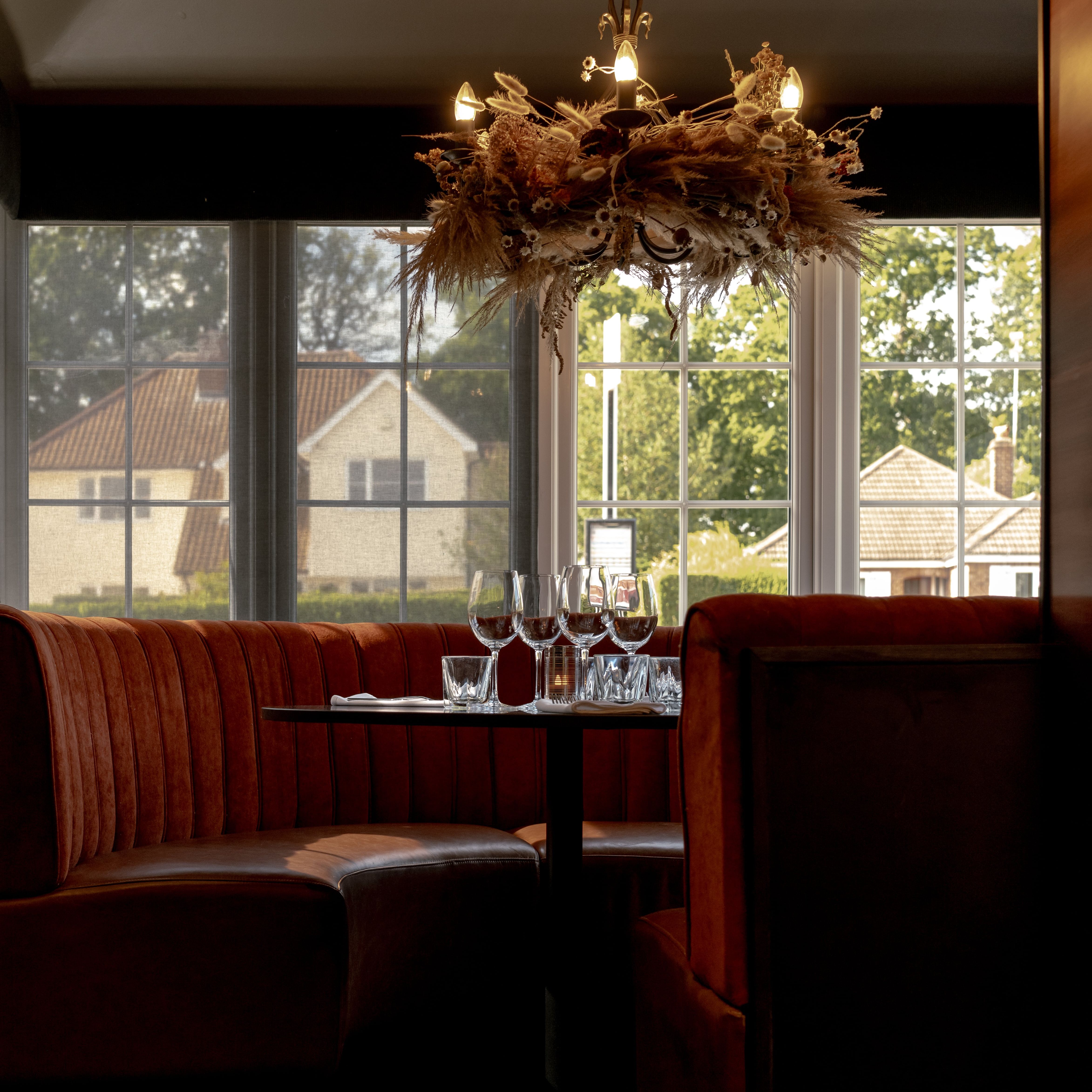 Elegant restaurant booth with red velvet seating, set table, and decorative chandelier