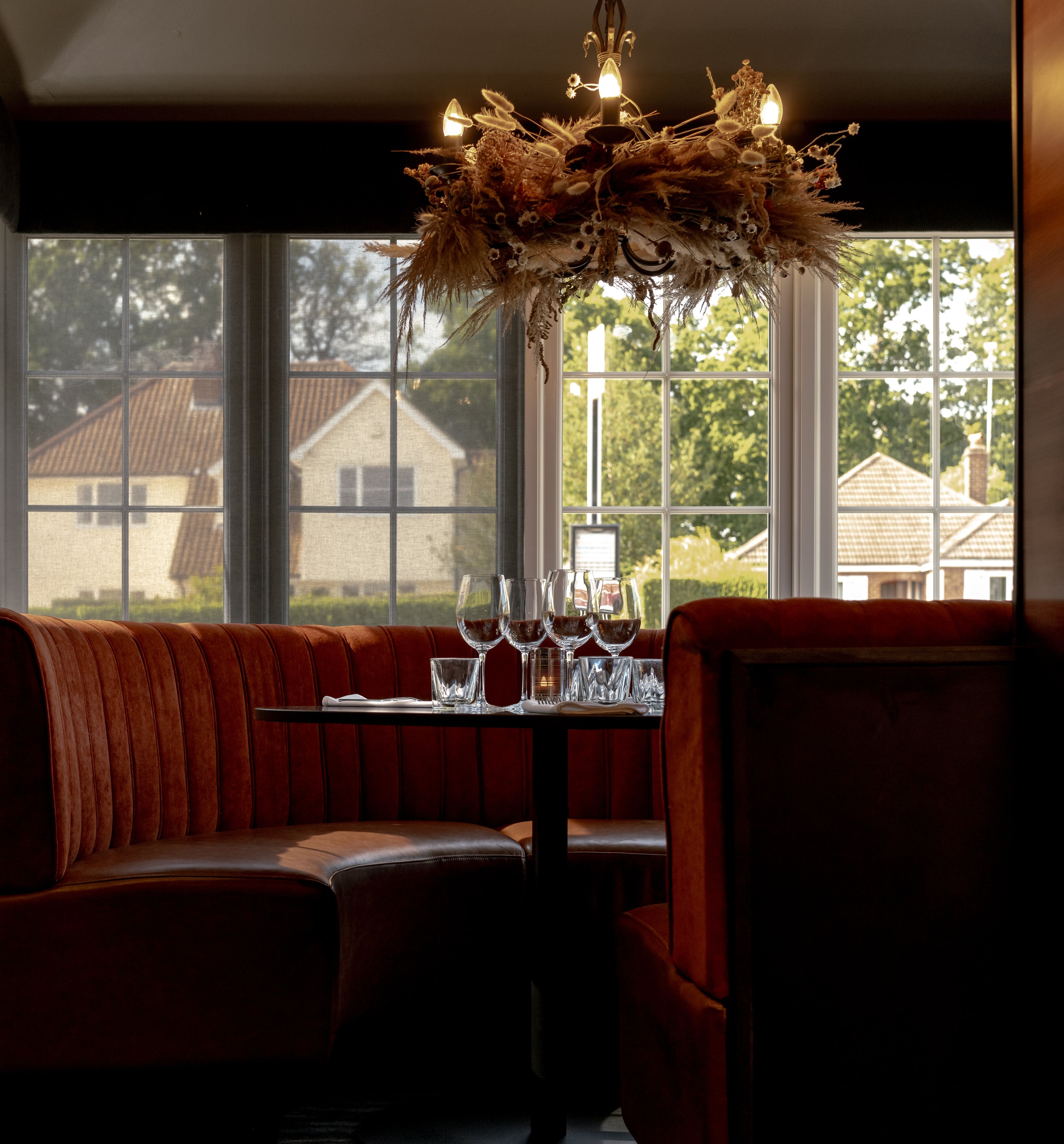 Elegant restaurant booth with red velvet seating, set table, and decorative chandelier