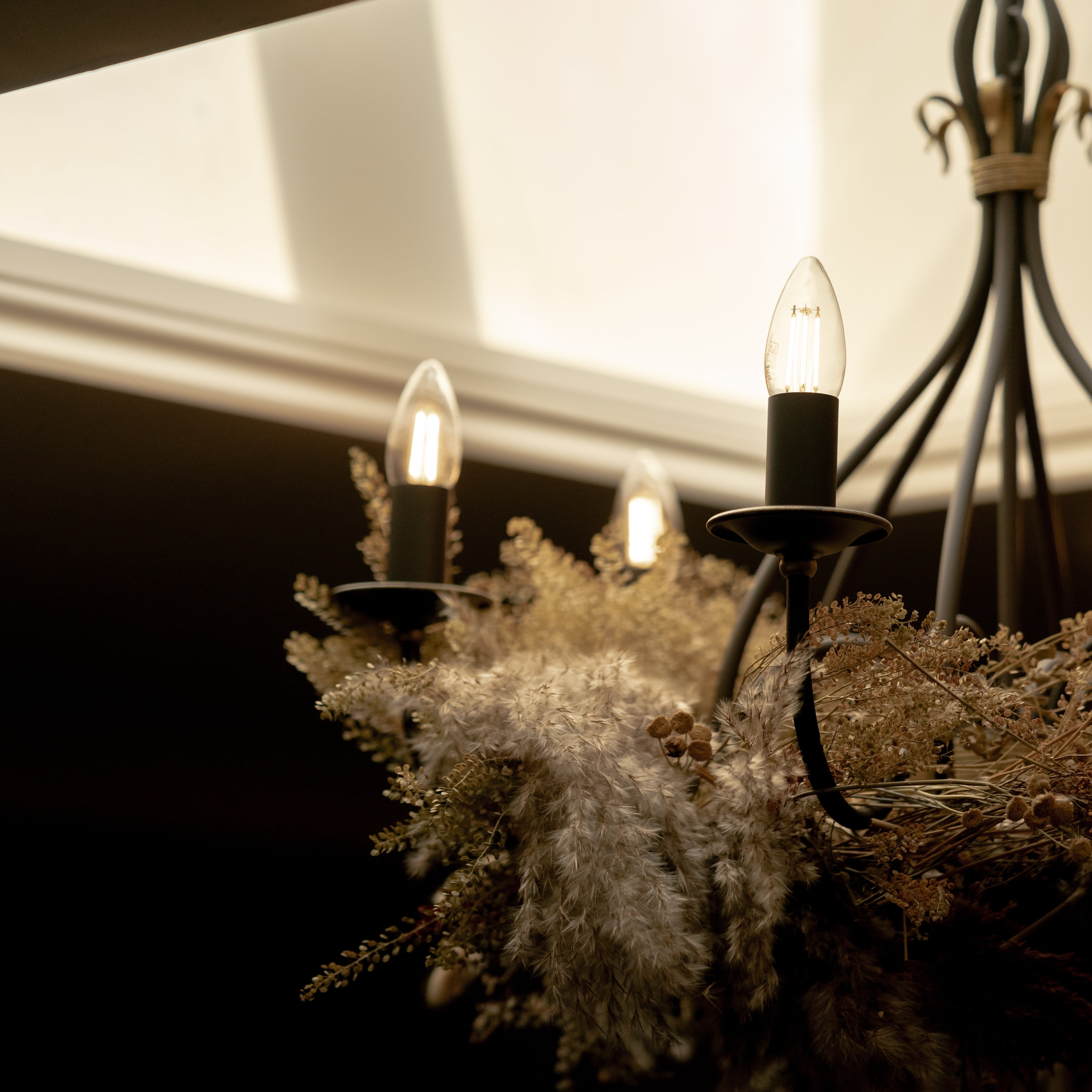 Decorative chandelier with glowing bulbs and dried floral arrangement